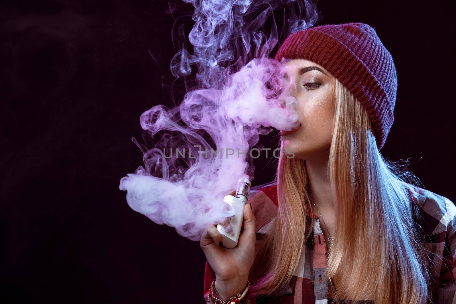 young woman smoking electronic cigarette on black background. Copy space