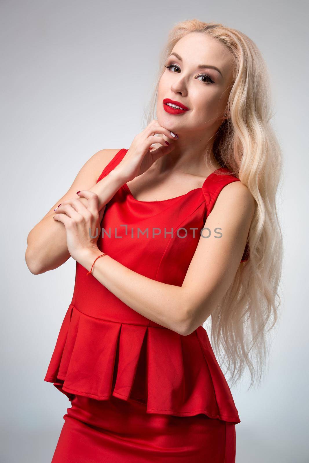Glamorous young woman in red dress on gray background. She looks into the camera