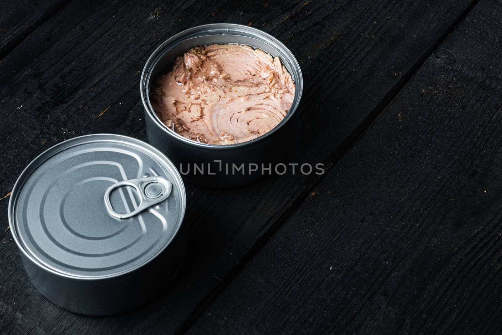 Canned Chunk Light Tuna set, in tin can, on black wooden table background, with copyspace and space for text