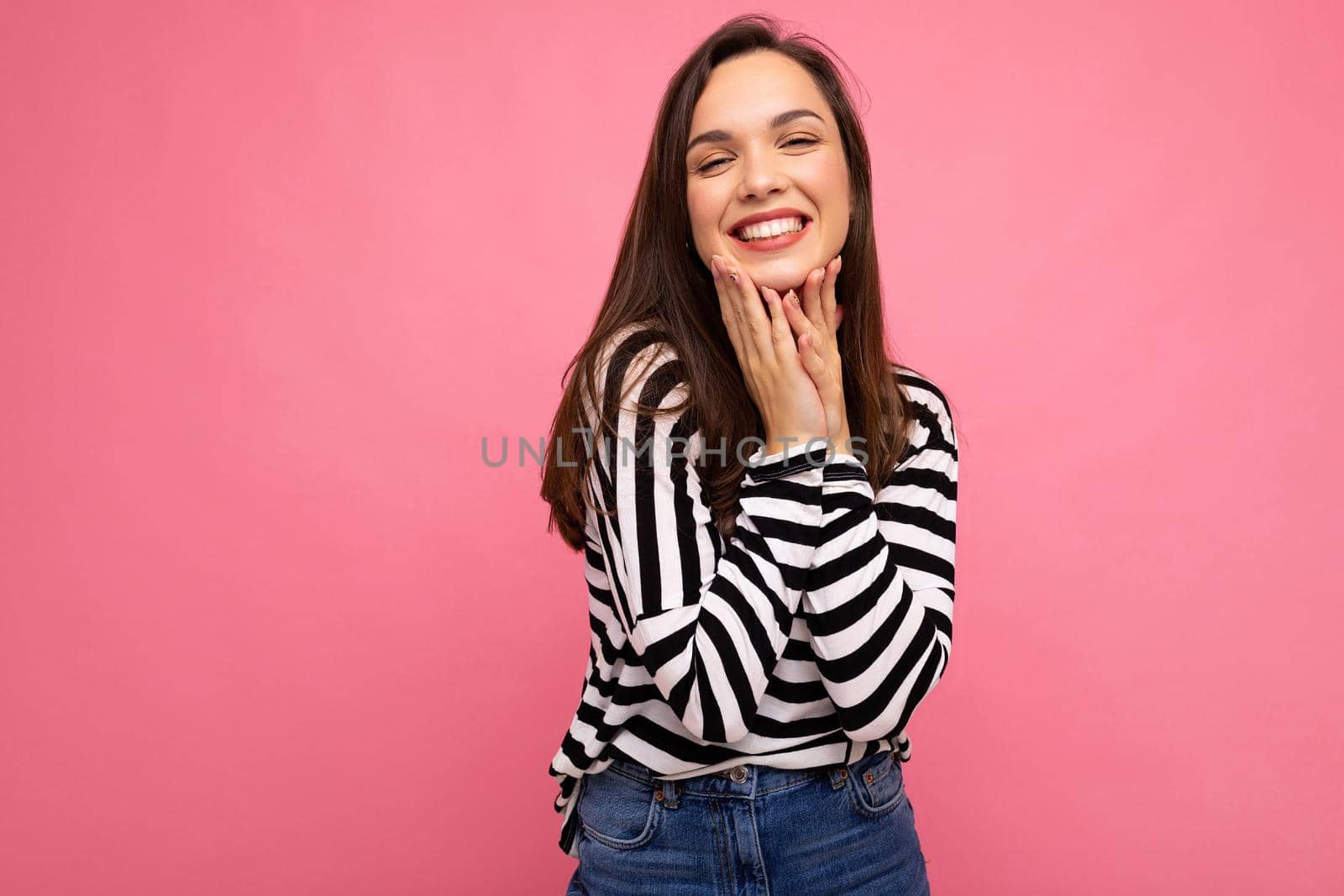 Photo of young smiling positive happy pretty brunette woman with sincere emotions wearing casual striped pullover isolated on pink background with copy space.