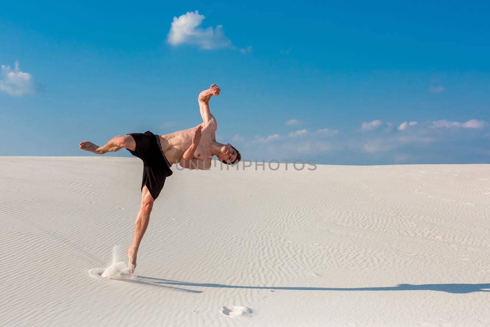 Portrait of young parkour man doing flip or somersault on the sand. Freezed moment of beginning doing bounce.