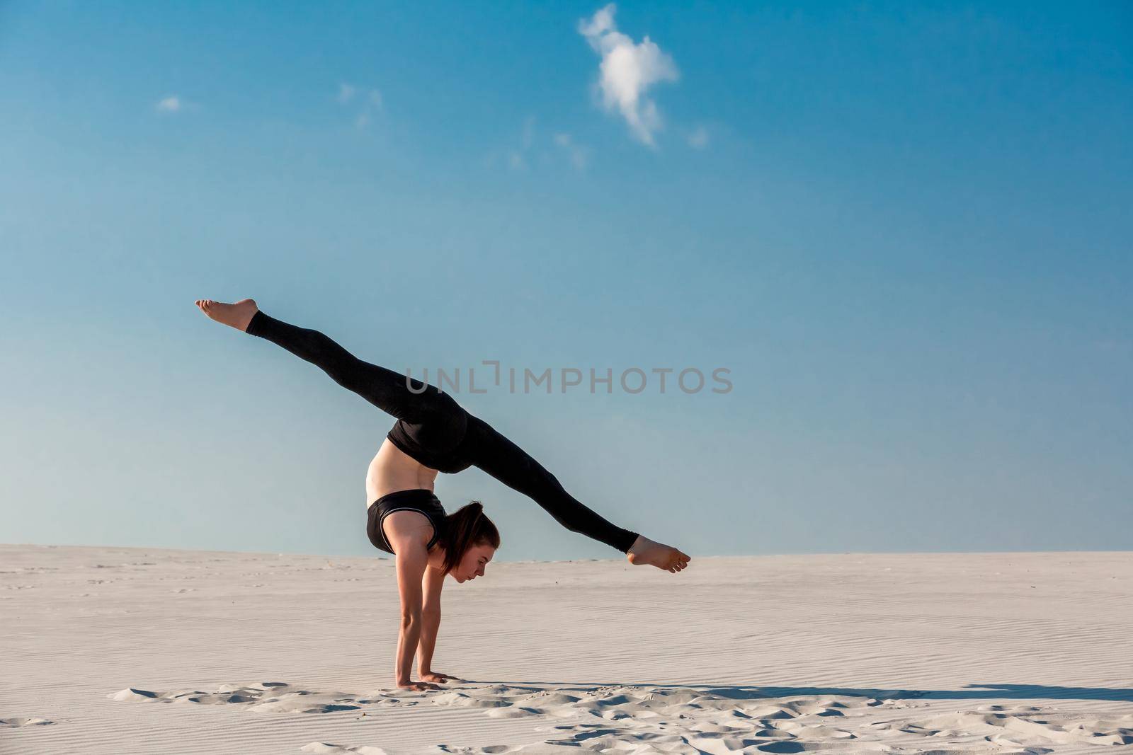 Young woman practicing handstand on beach with white sand and bright blue sky by nazarovsergey