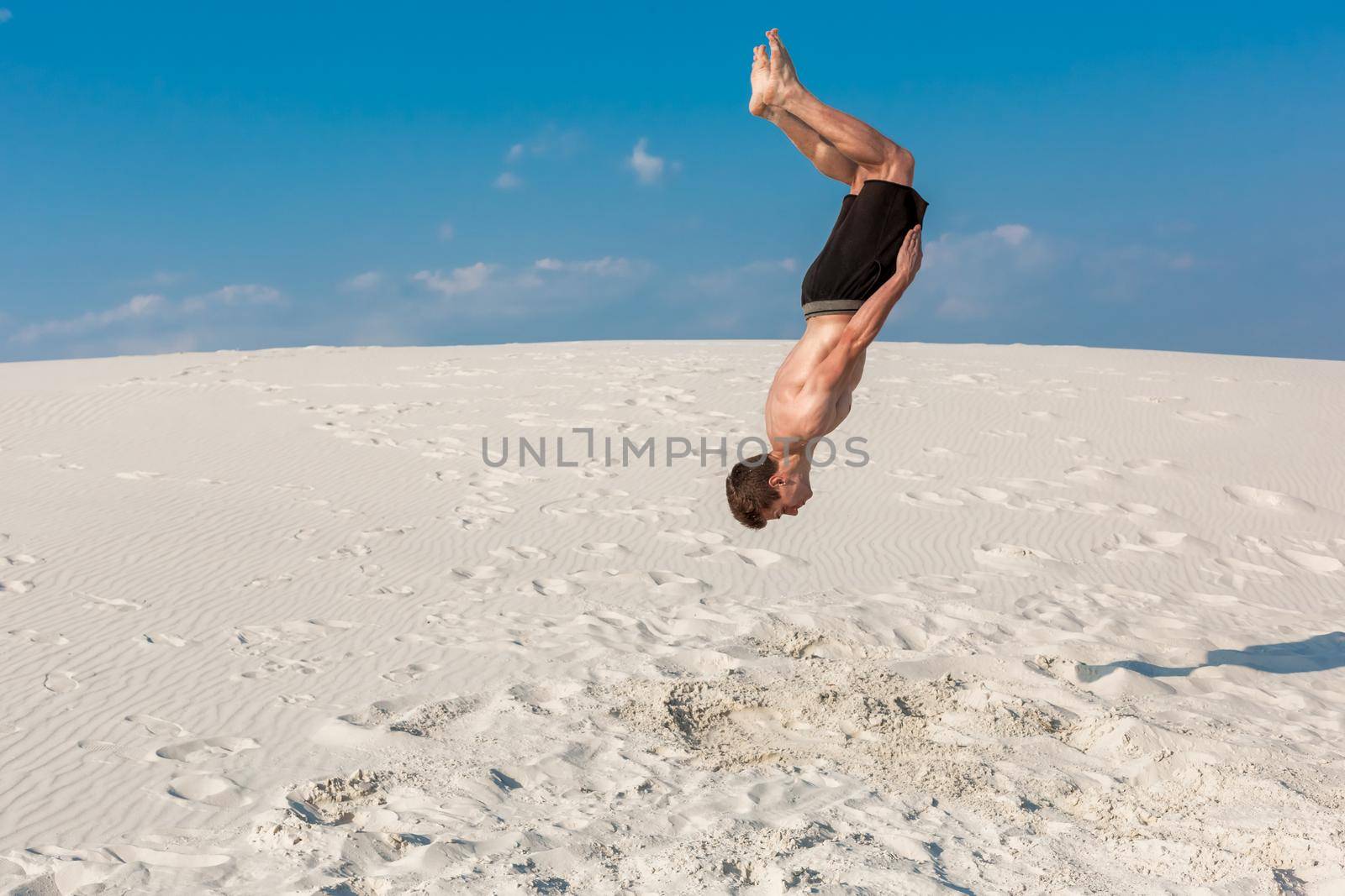 Portrait of young parkour man doing flip or somersault on the sand. by nazarovsergey