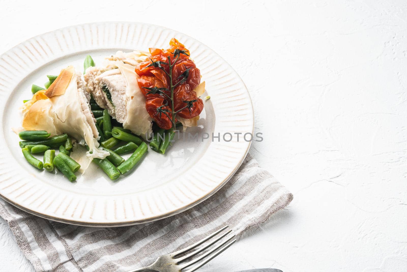 Stuffed chicken meat with filo set, with baked cherry tomatoes And green beans, on white stone background, with copy space for text