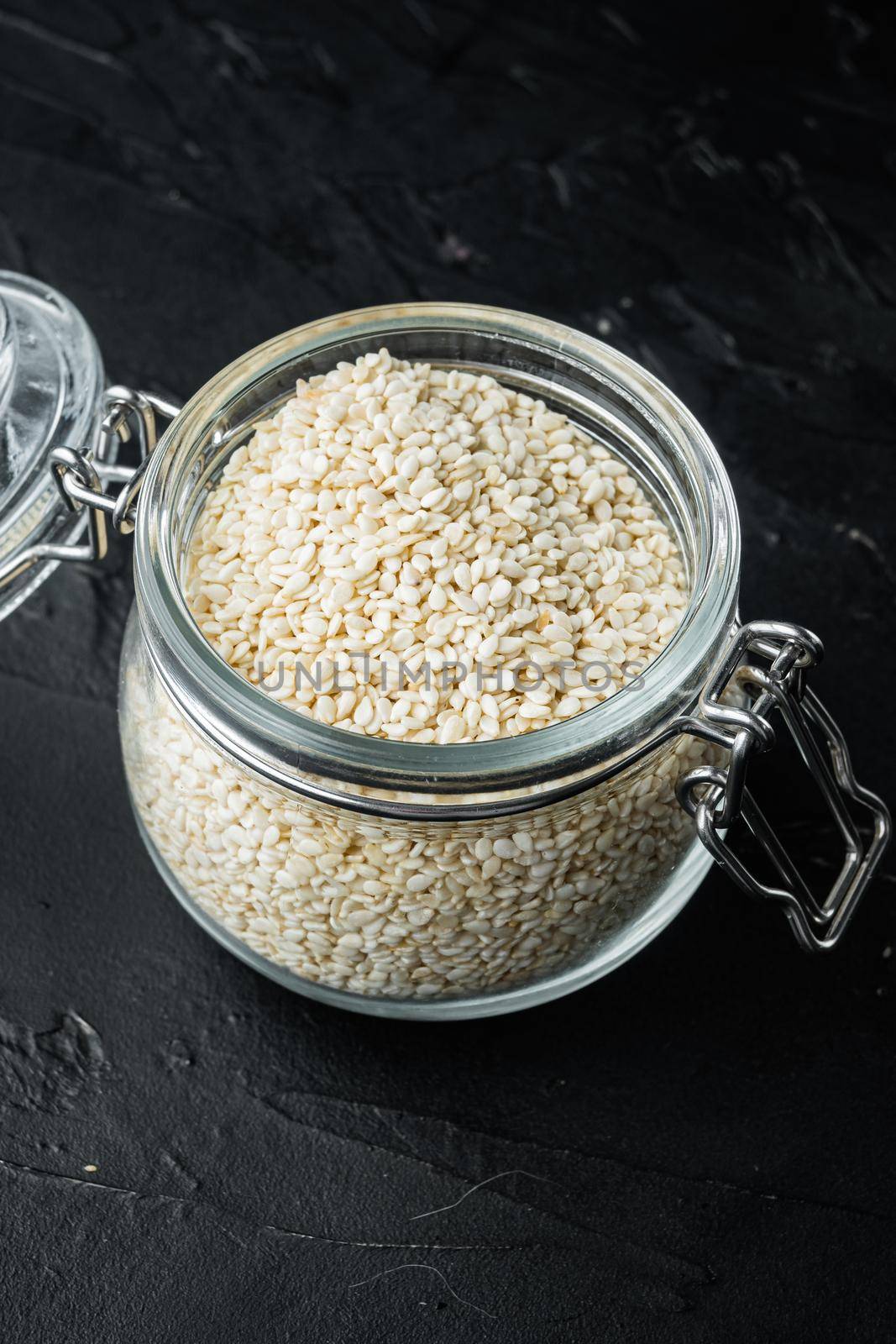 Decorticated sesame seeds set, in glass jar, on black stone background