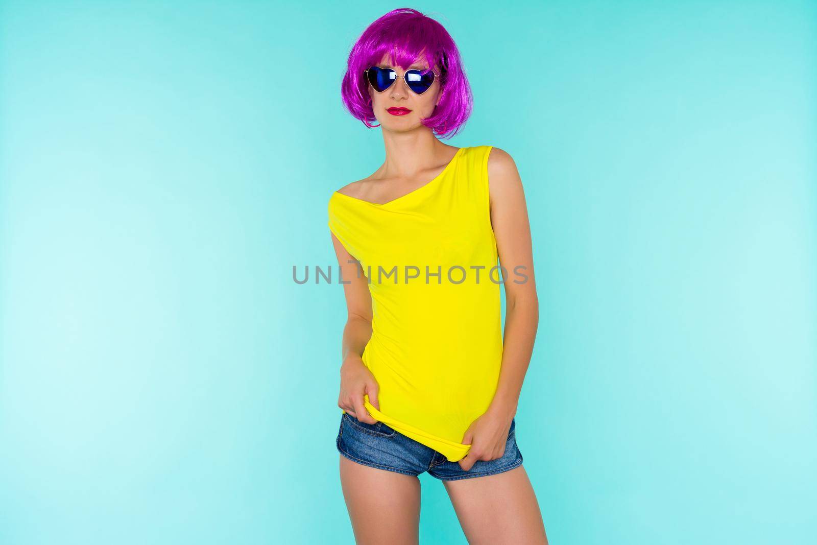 Portrait of young transgender woman in pink wig and sunglasses, yellow t-shirt on blue background by zartarn