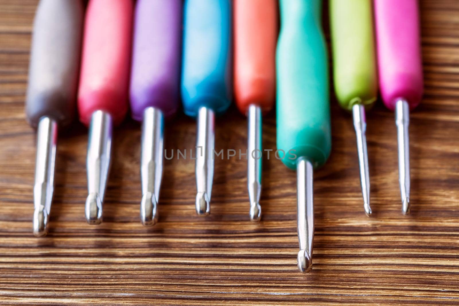 A set of multicolored crochet hooks on a wooden background. Close-up, selective focus by marketlan
