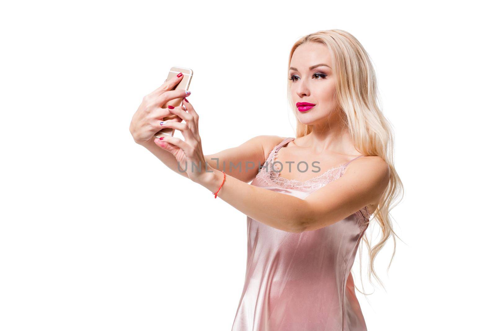 Young blonde doing selfie on isolated white background. Selfie time. Young beautiful woman in silk dress