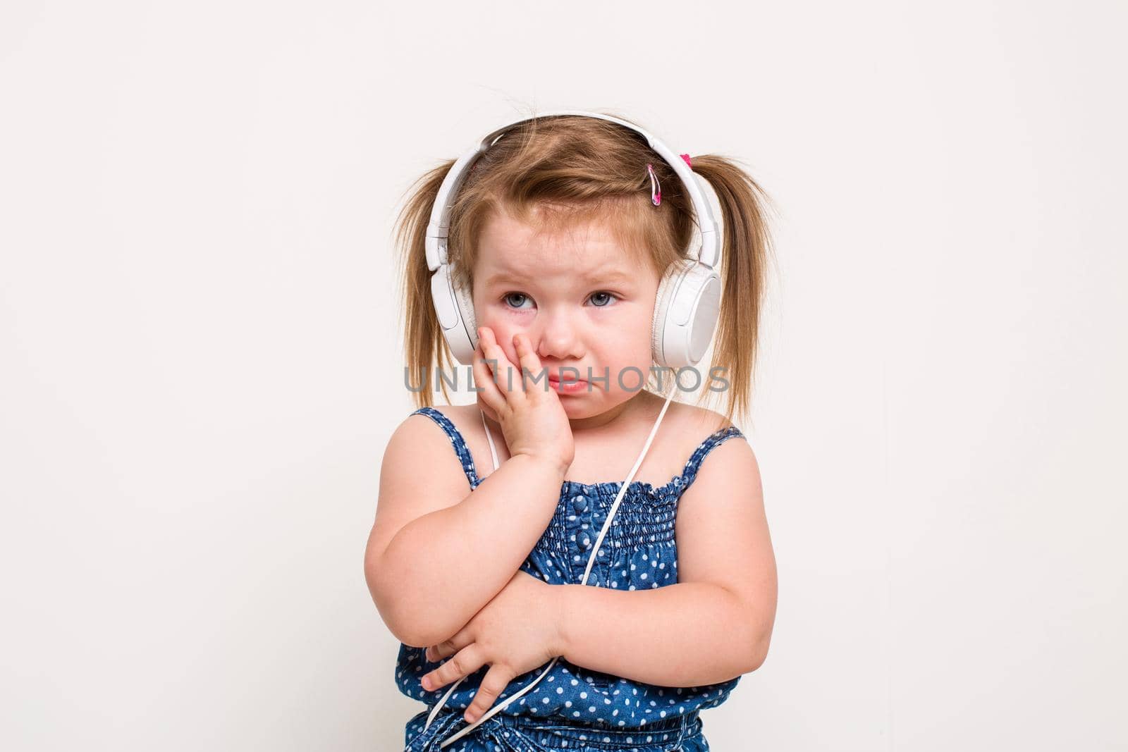 Cute little girl in headphones listening to music using a tablet on white background. The child does not look at the camera