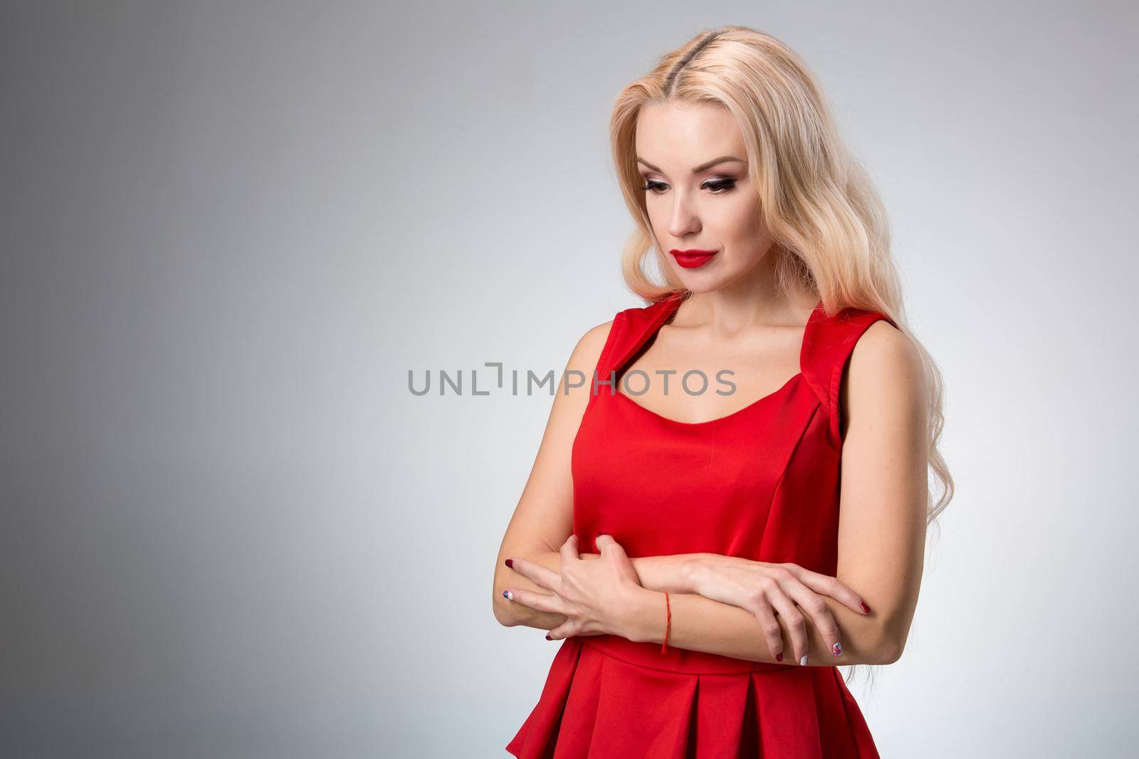 Glamorous young woman in red dress on gray background.