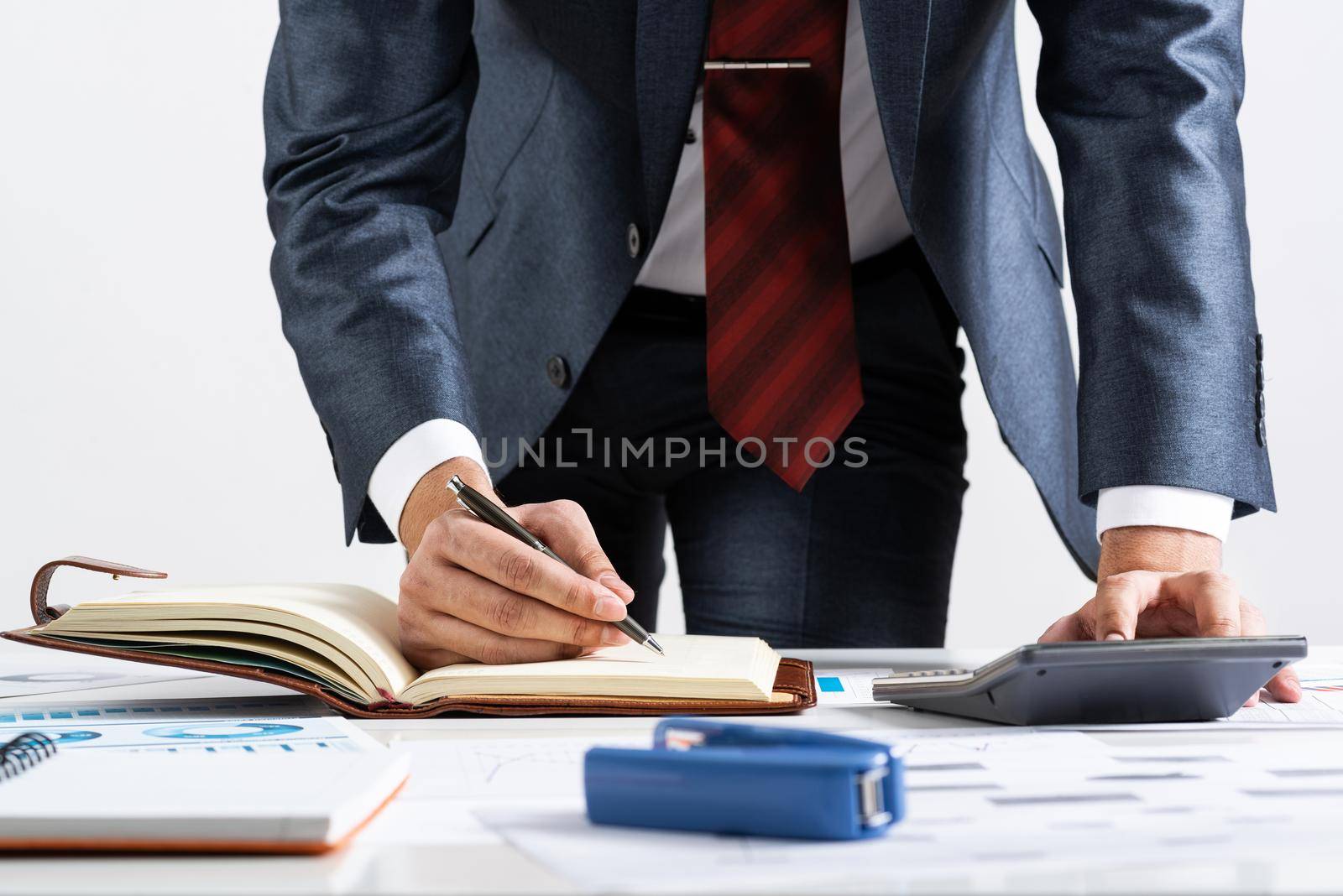 Close-up businessman hand writing to do list in diary at desk. Financial expertise and consulting. Manager in suit and tie planning day with personal organizer. Time management and work organization.