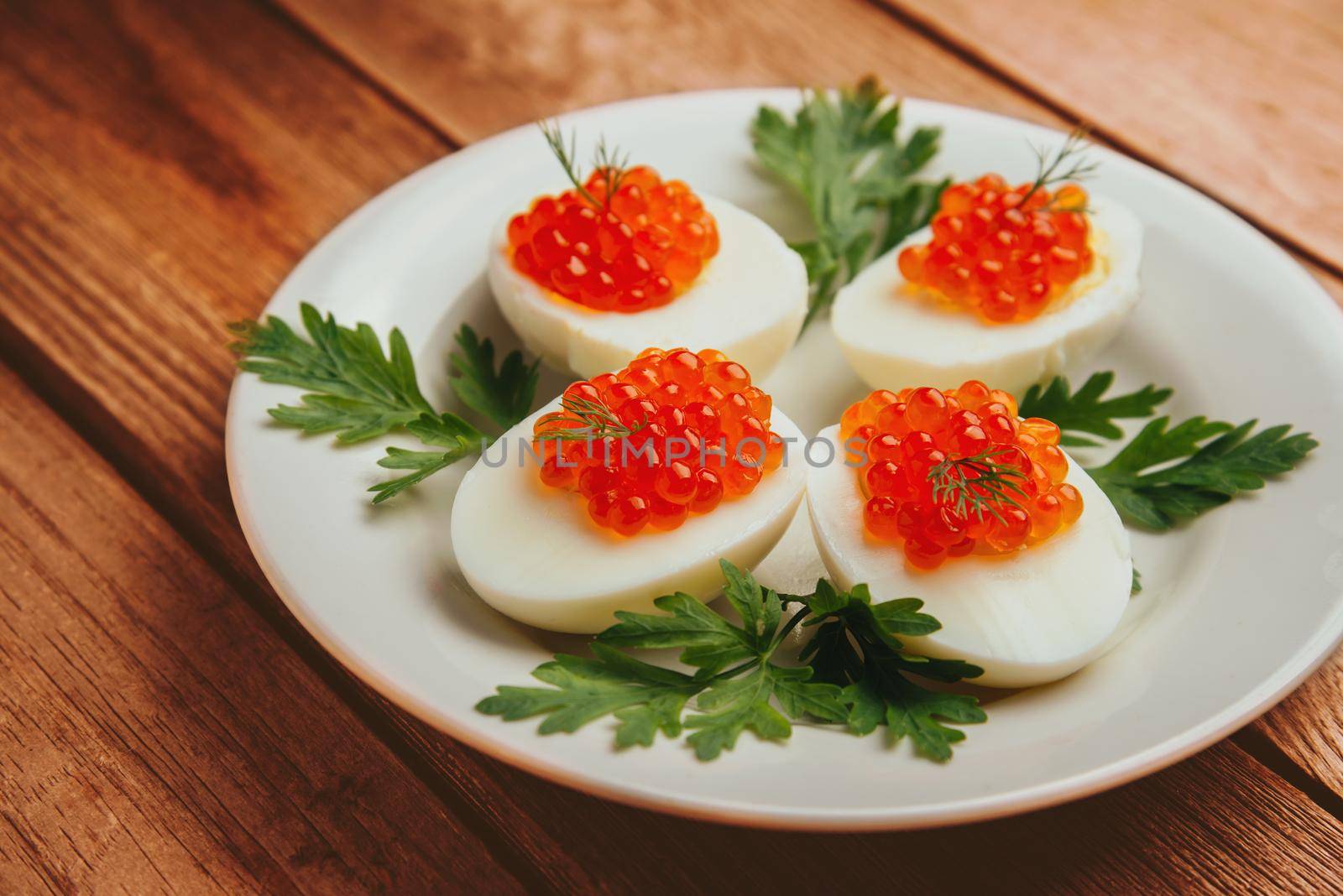 Dish boiled eggs with red salmon caviar and parsley on plate on a wooden background