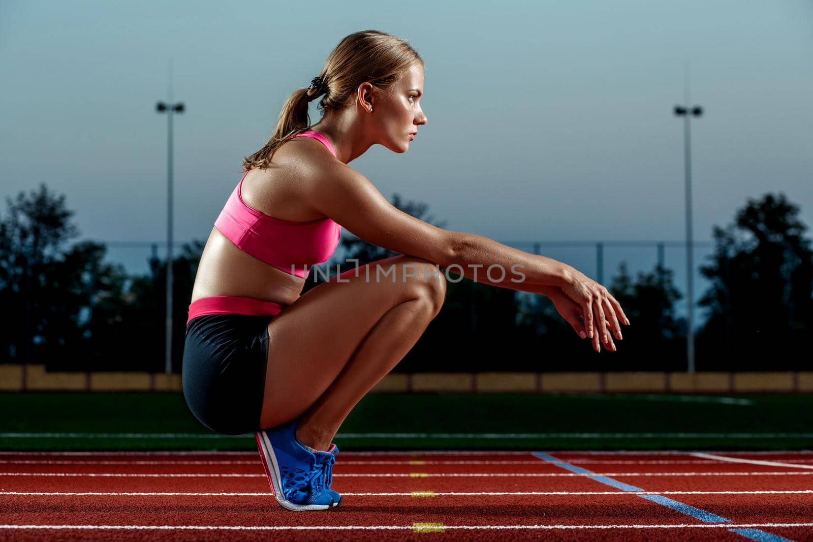 Picture of beautiful young European female runner or sprinter sitting on outdoor stadium track, feeling exhausted after sprint or marathon. by nazarovsergey