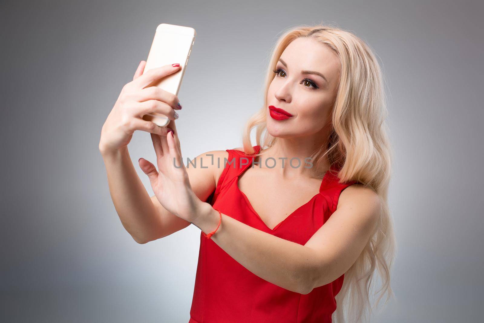 Portrait of a Beautiful successful smiling girl doing selfie in red dress on light background by nazarovsergey