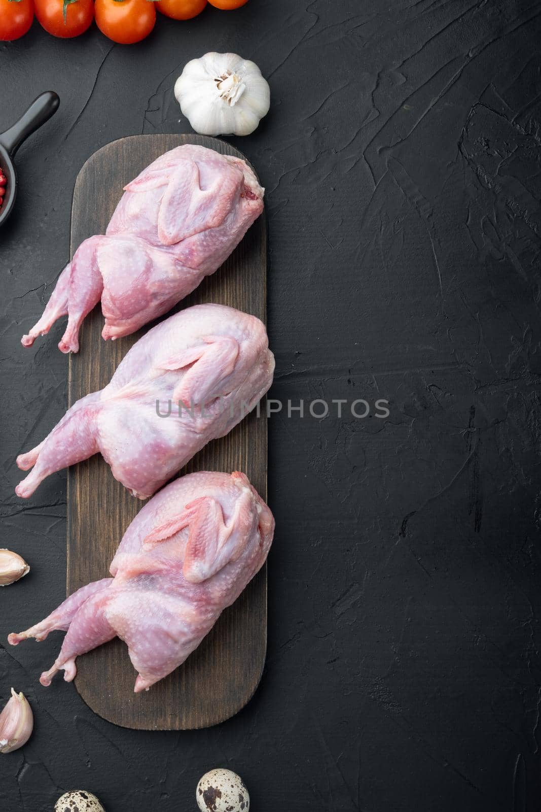 Whole quails meat with spices, herbs, vegetables, top view, on black textured background with copy space