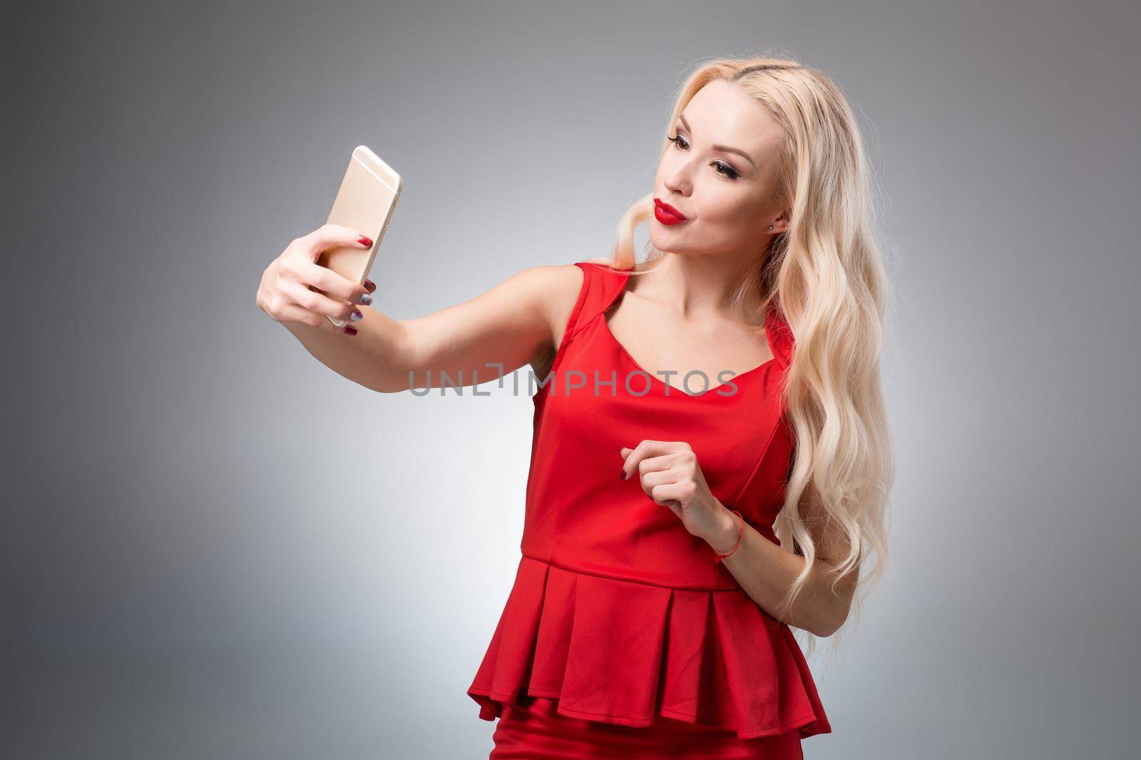 Portrait of a Beautiful successful blonde doing selfie in a red dress on a light background