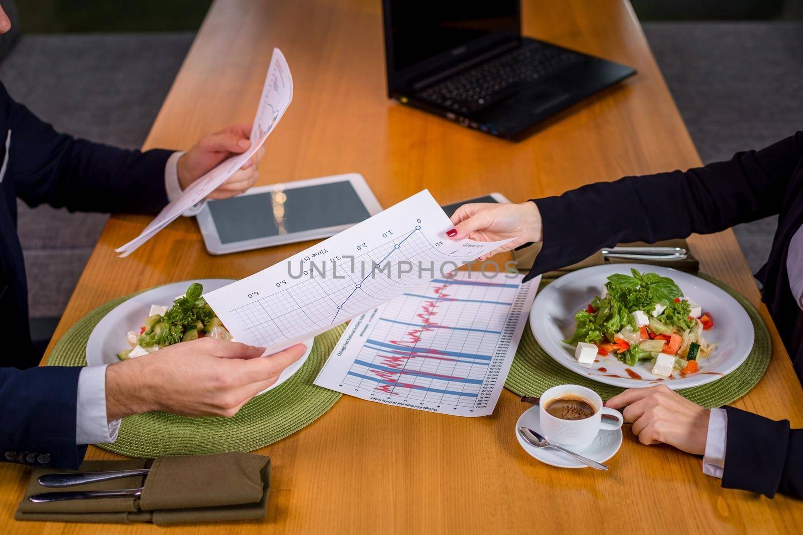 A woman and a man on a business lunch in a restaurant. They pass each other data and graphs