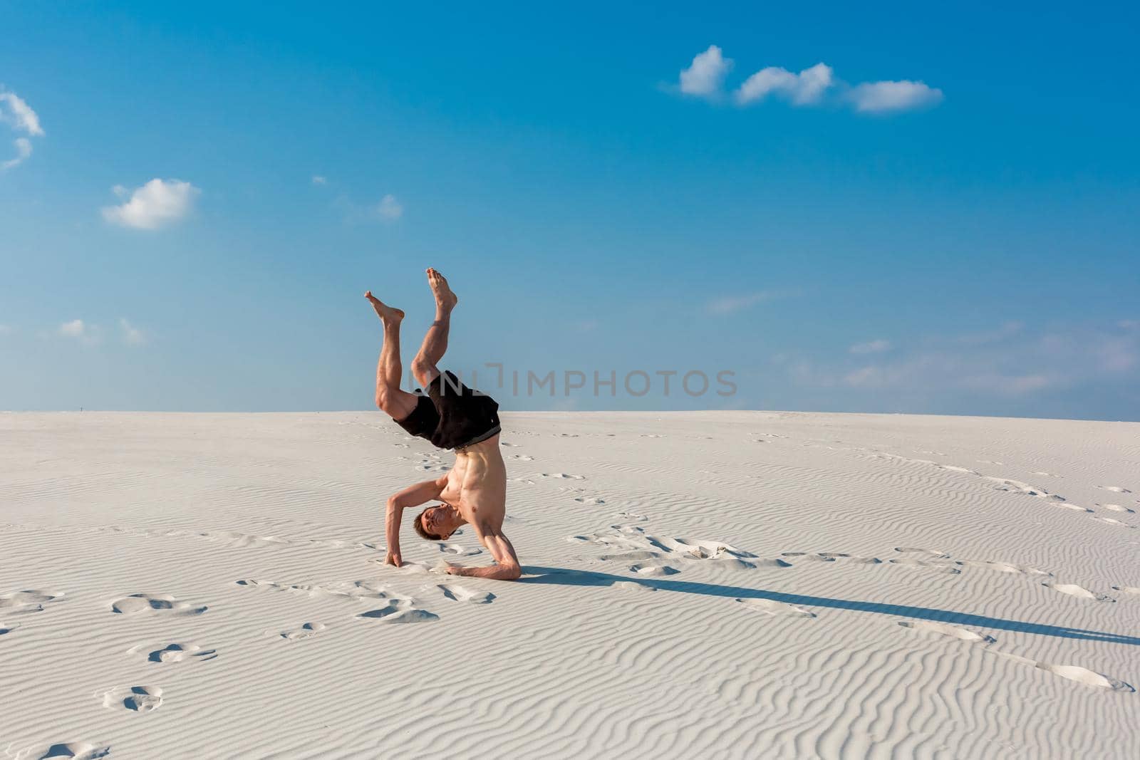 Young sporty man want doing acrobatic exercises on the sand near river. Portrait of young parkour man