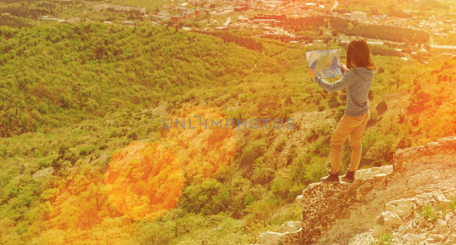 Hiker young woman standing with a map in the mountains in summer. Image with sunlight effect