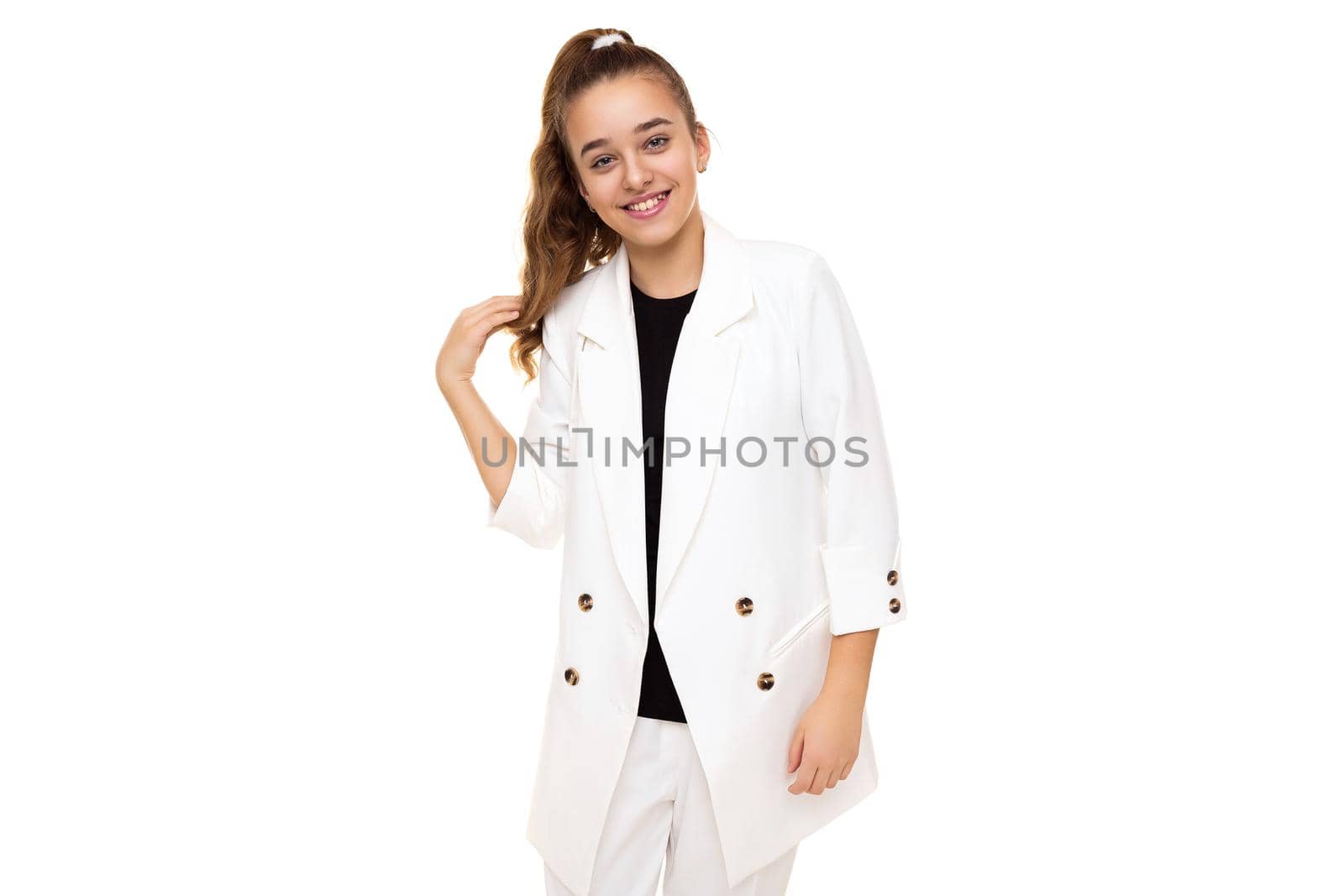 Photo of beautiful cute adorable positive smiling brunette teenage girl with ponytail in stylish white jacket and white pants isolated on white background with copy space for text.