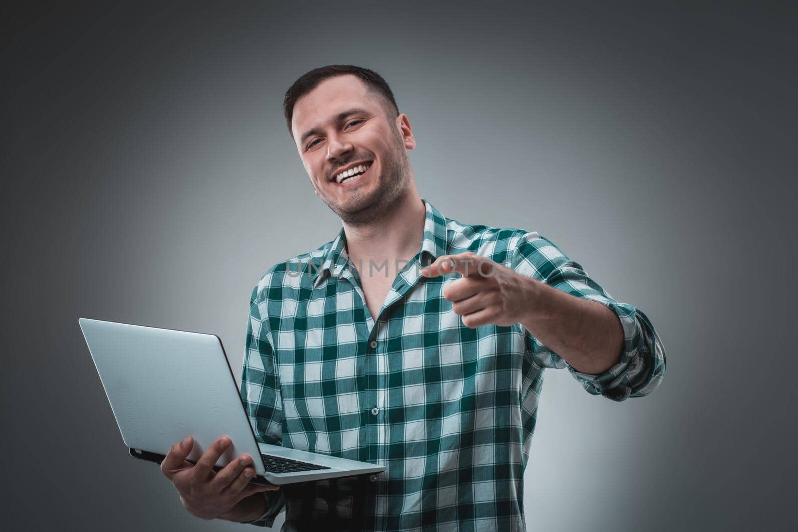 Attractive business man model in green shirt isolated on gray working with laptop, showing something by left hand. by nazarovsergey