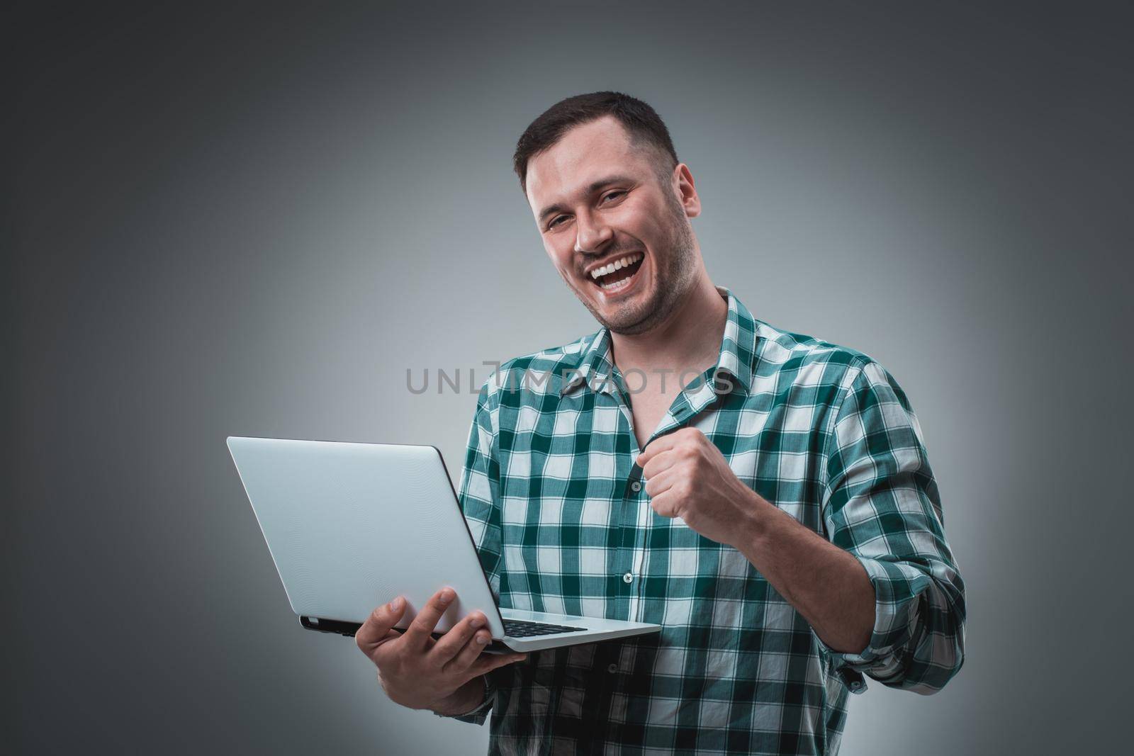 Attractive business man model in green shirt isolated on gray working with laptop, showing something by left hand. by nazarovsergey