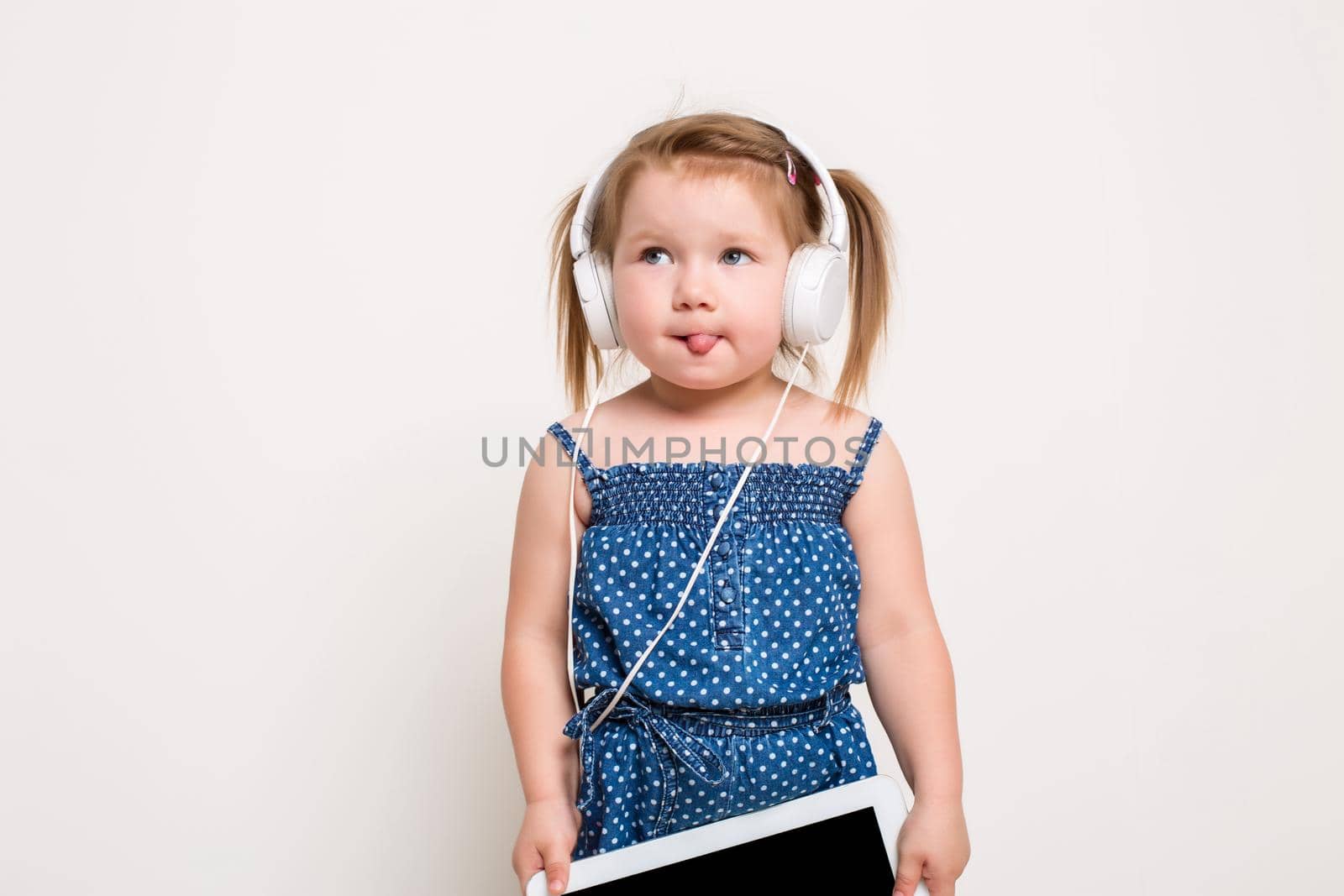 Cute little girl in headphones listening to music using a tablet and smiling on white background by nazarovsergey