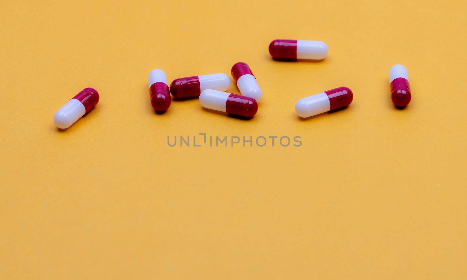 Antibiotic capsule pills on yellow background. Pharmaceutical industry. Prescription drug. Red-white capsule pills. Pharmaceutical product. Pharmacy web banner. Health insurance and health budget.