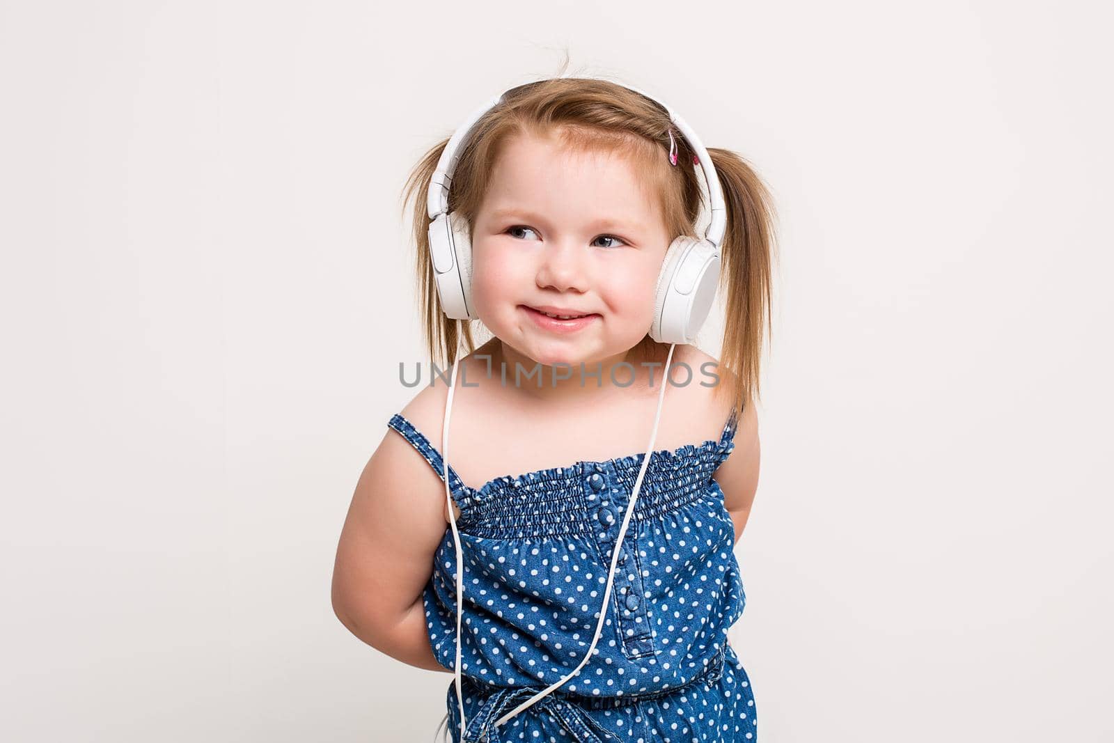 Cute little girl in headphones listening to music using a tablet and smiling on white background. The child does not look at the camera