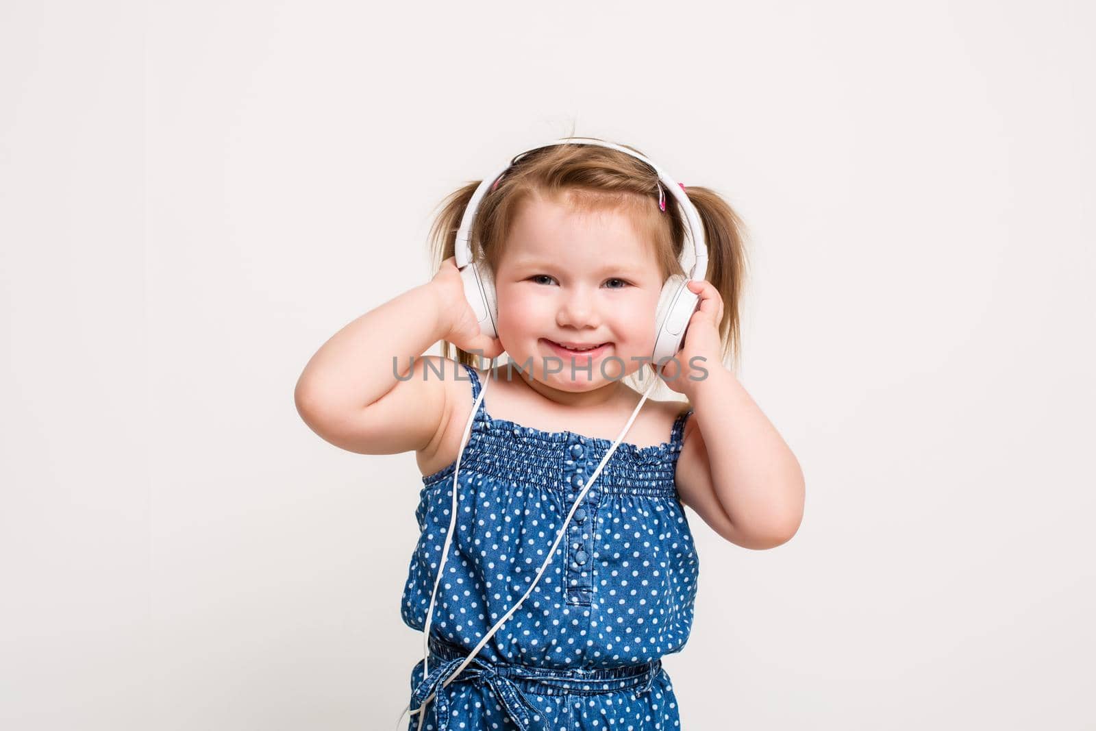 Cute little girl in headphones listening to music using a tablet and smiling on white background. A child looks at the camera