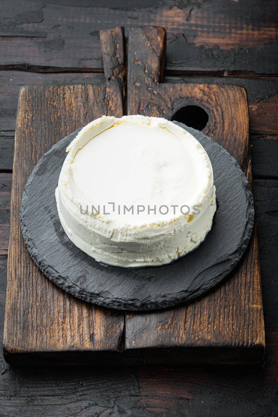 A fresh, ricotta cheese, on wooden cutting board, on old dark wooden table background
