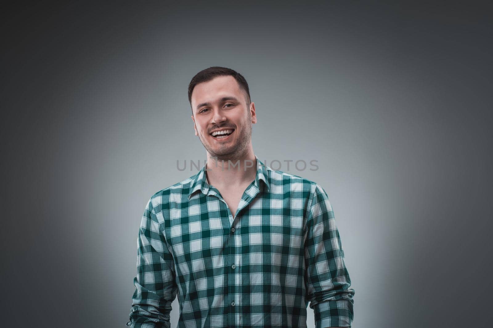 Cheerful man laughing and looking at camera with a big grin. Portrait of a happy young man standing over grey background.