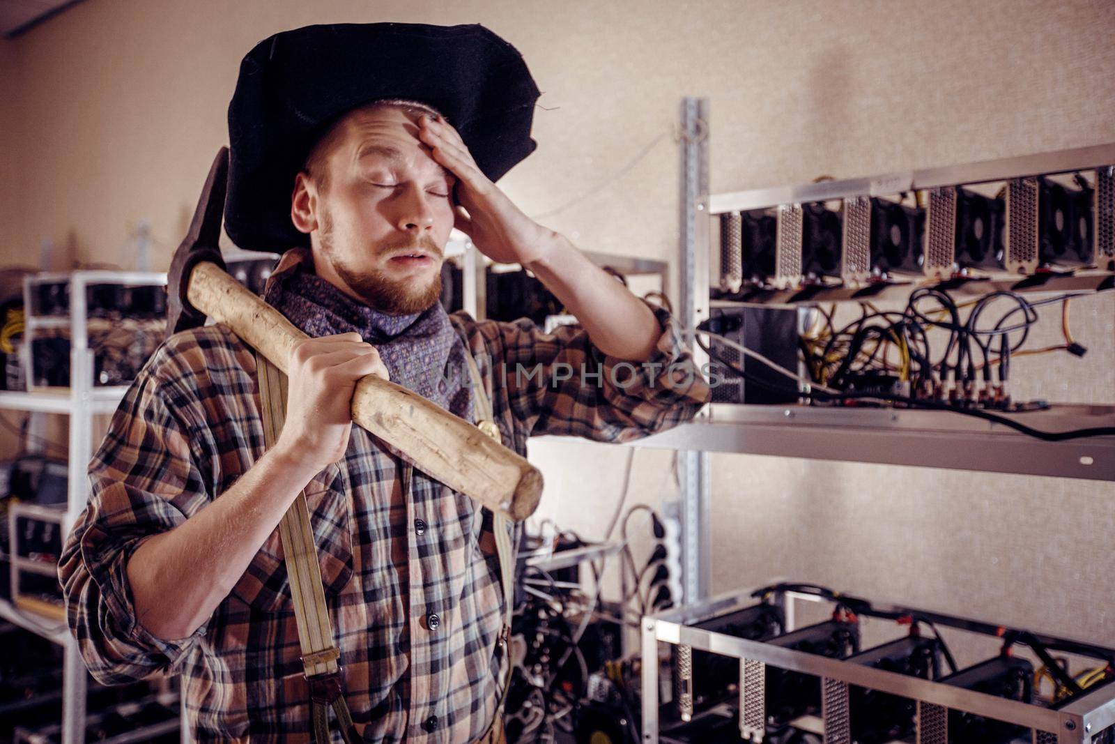 A man holds his forehead with a tool in his hand against the background of computer devices