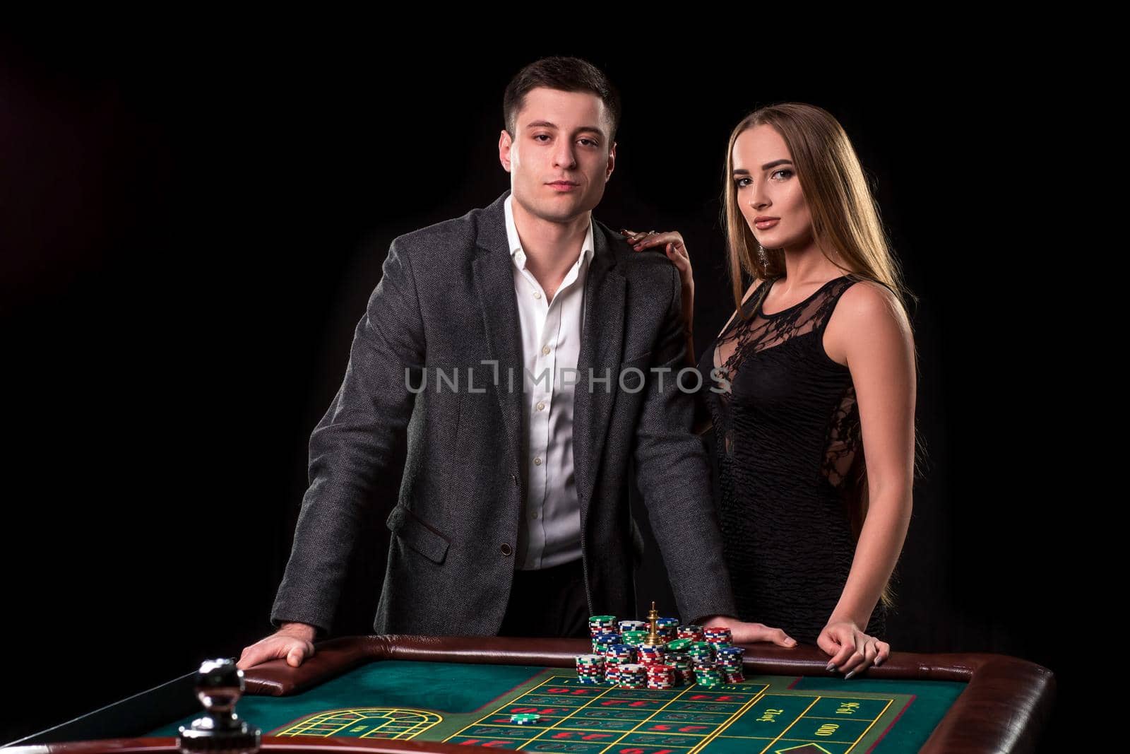 Elegant couple at the casino betting on the roulette, on a black background. A man in a suit with a beautiful young woman in a black dress