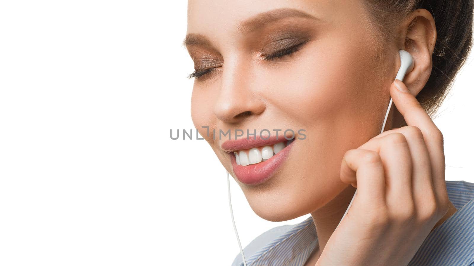 Close up portrait of a smiley young woman listening to the music via earphones.
