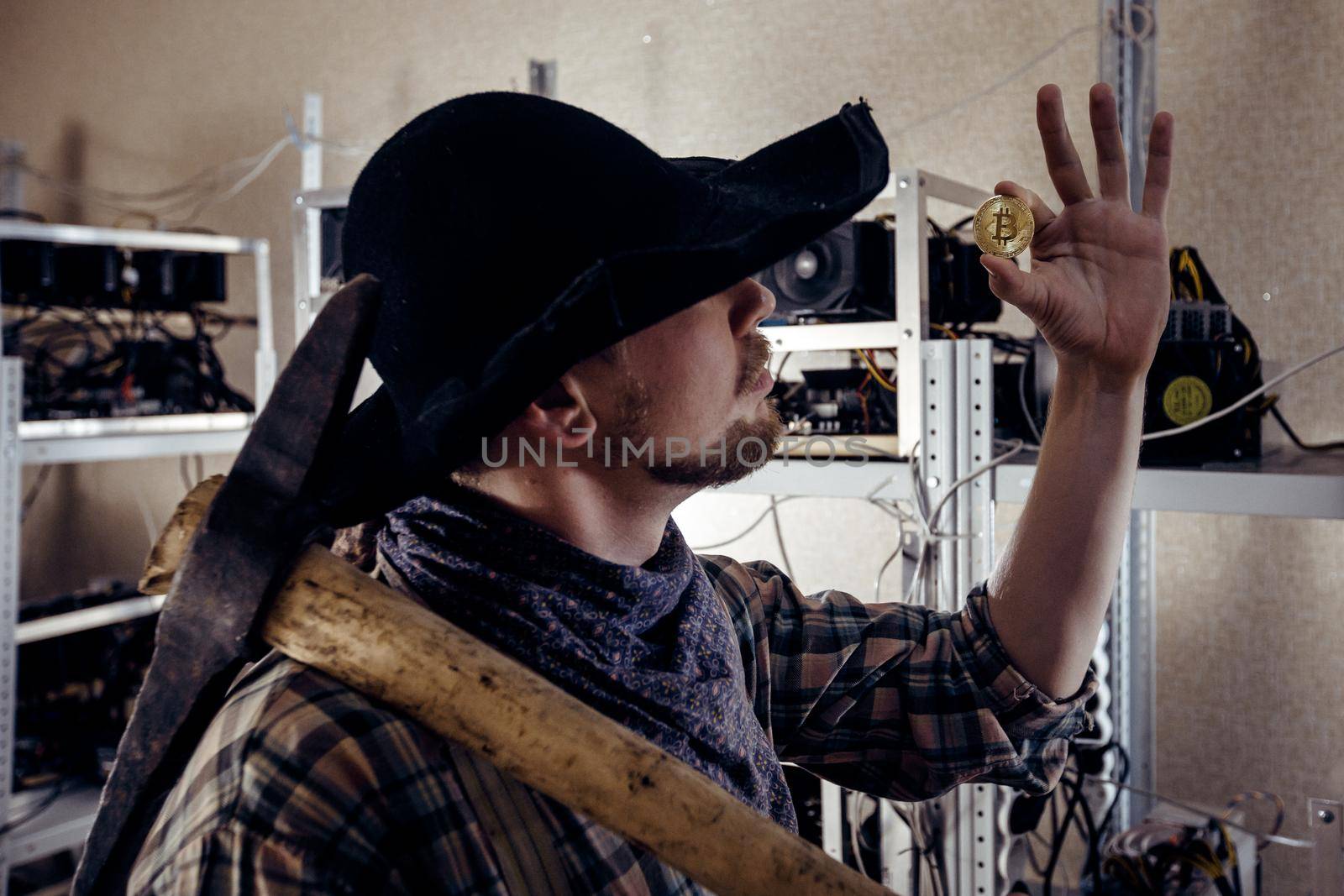 A man in working clothes with a tool on his shoulder examines a gold coin