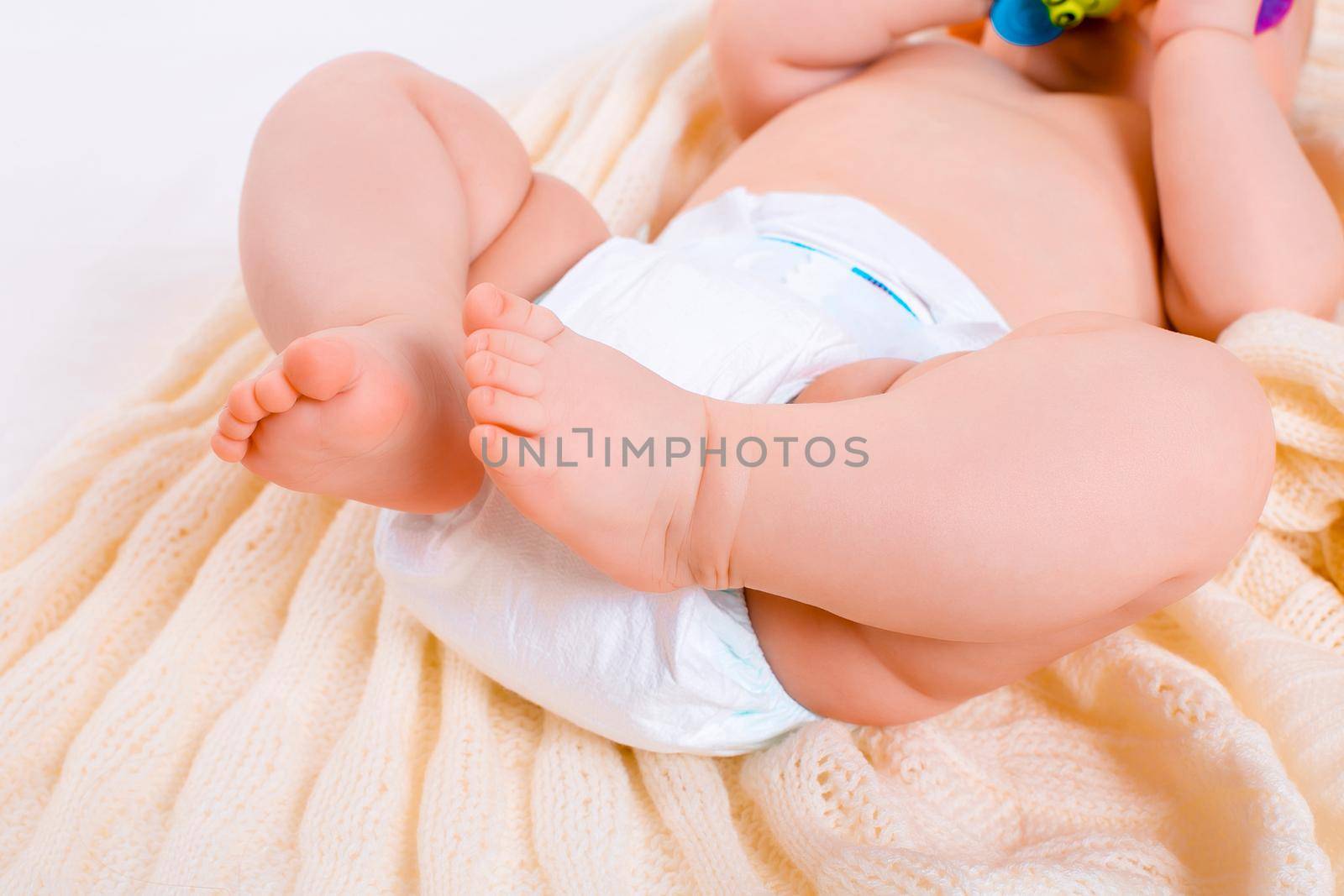 feet of a six months old baby wearing diapers lying in bed at home