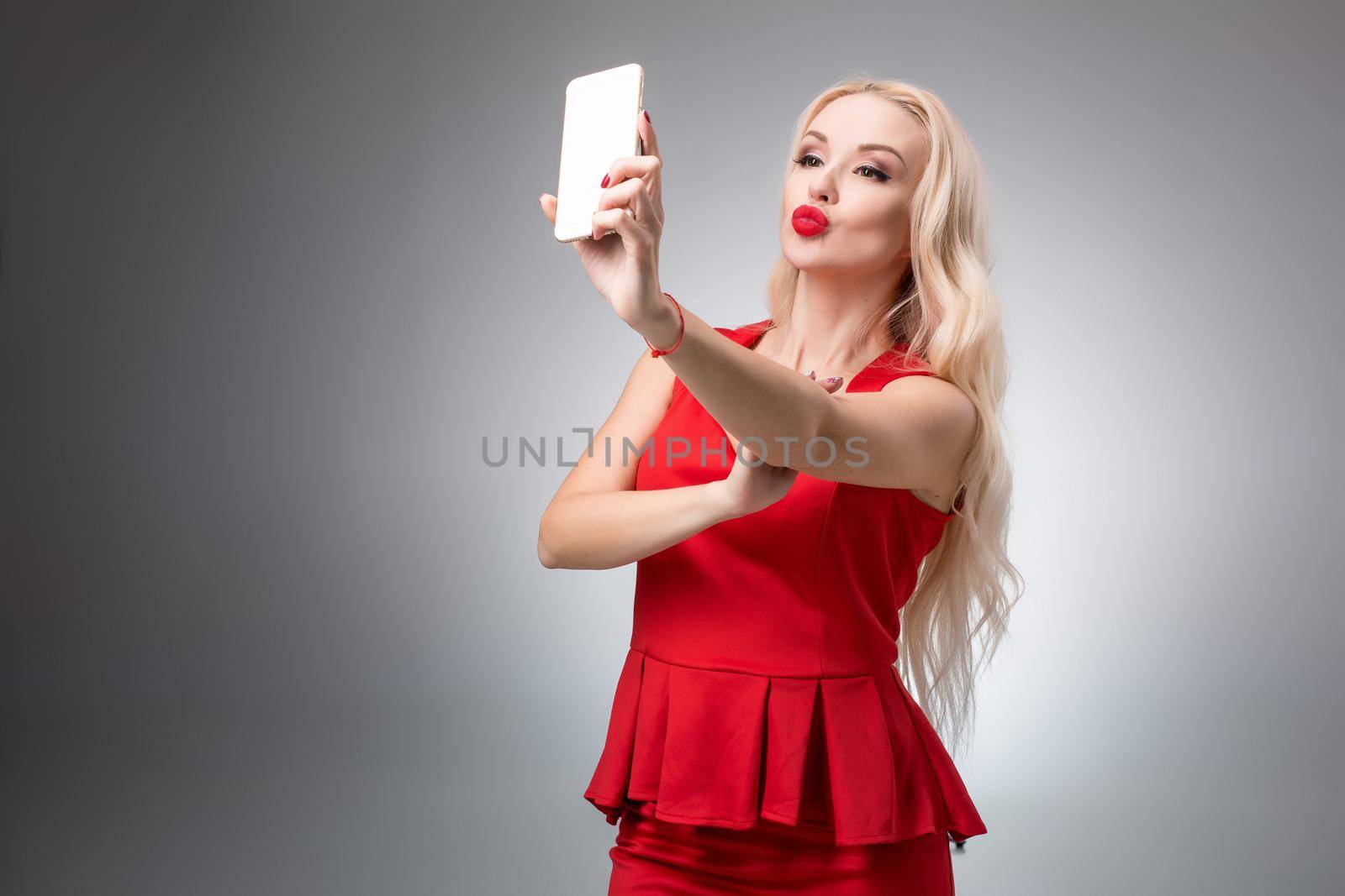 Portrait of a Beautiful successful blonde doing selfie in a red dress on a light background
