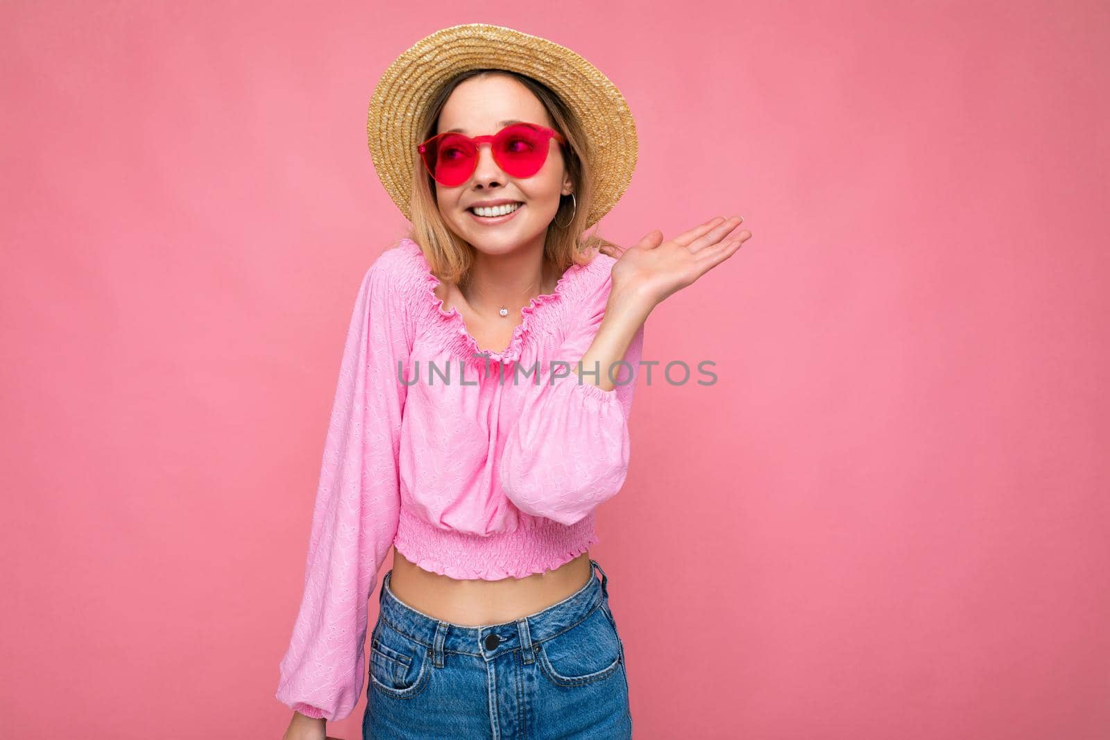 Photo shot of beautiful positive young blonde woman wearing summer casual clothes and stylish sunglasses isolated over colorful background looking to the side.