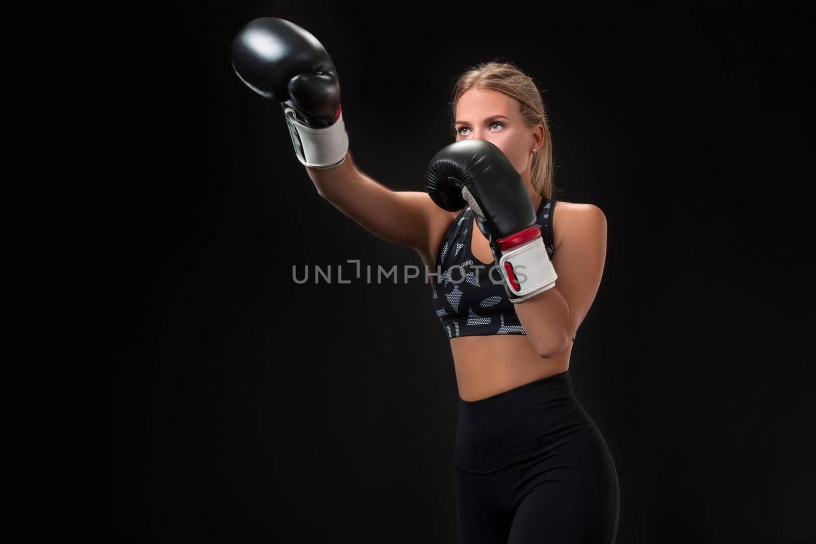 Beautiful female athlete in boxing gloves, in the studio on a black background. The boxer fulfills the blow