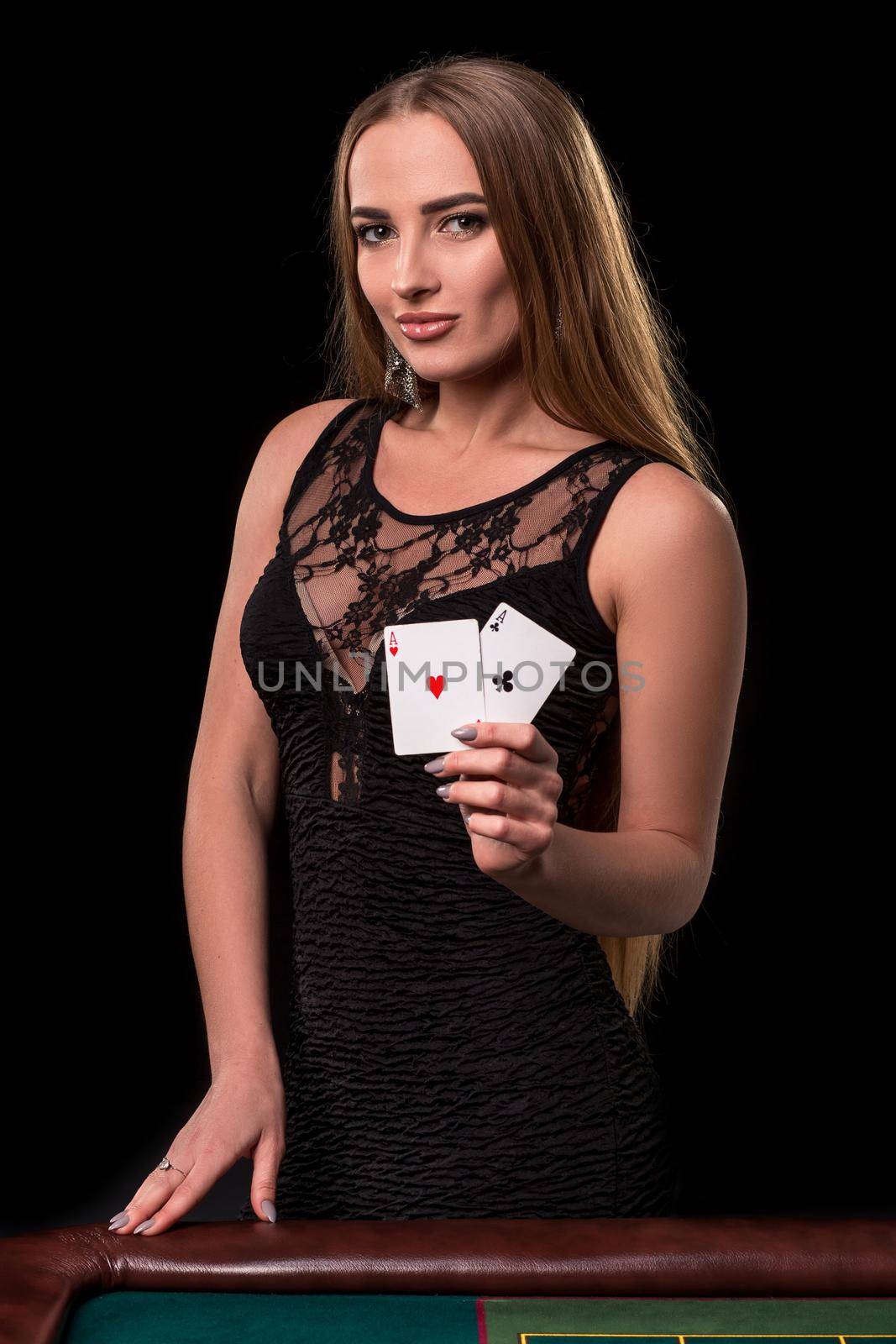 Young beautiful woman in a sexy black dress playing in casino. Girl holding the winning combination of poker cards on a black background. Two aces