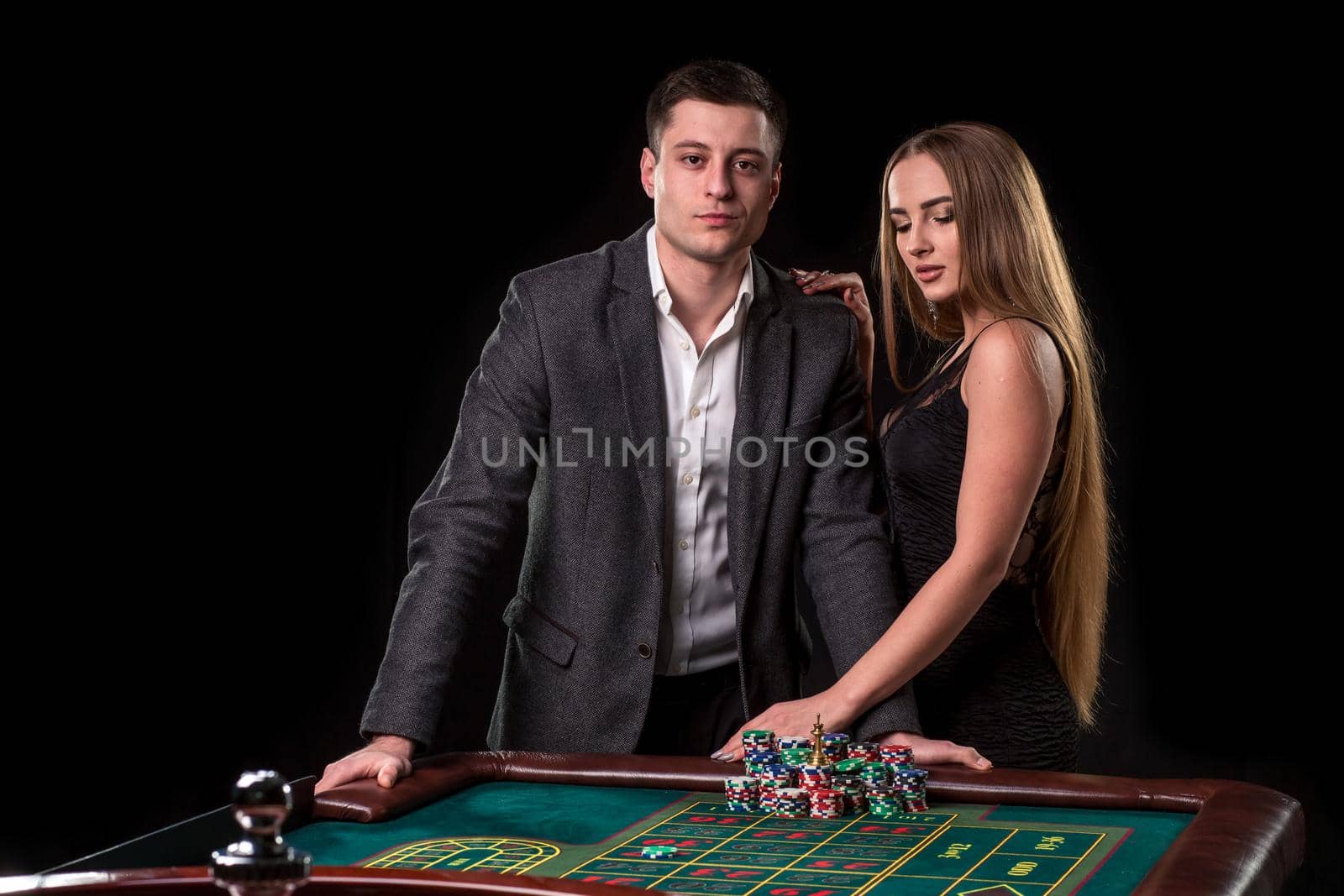 Elegant couple at the casino betting on the roulette, on a black background. A man in a suit with a beautiful young woman in a black dress