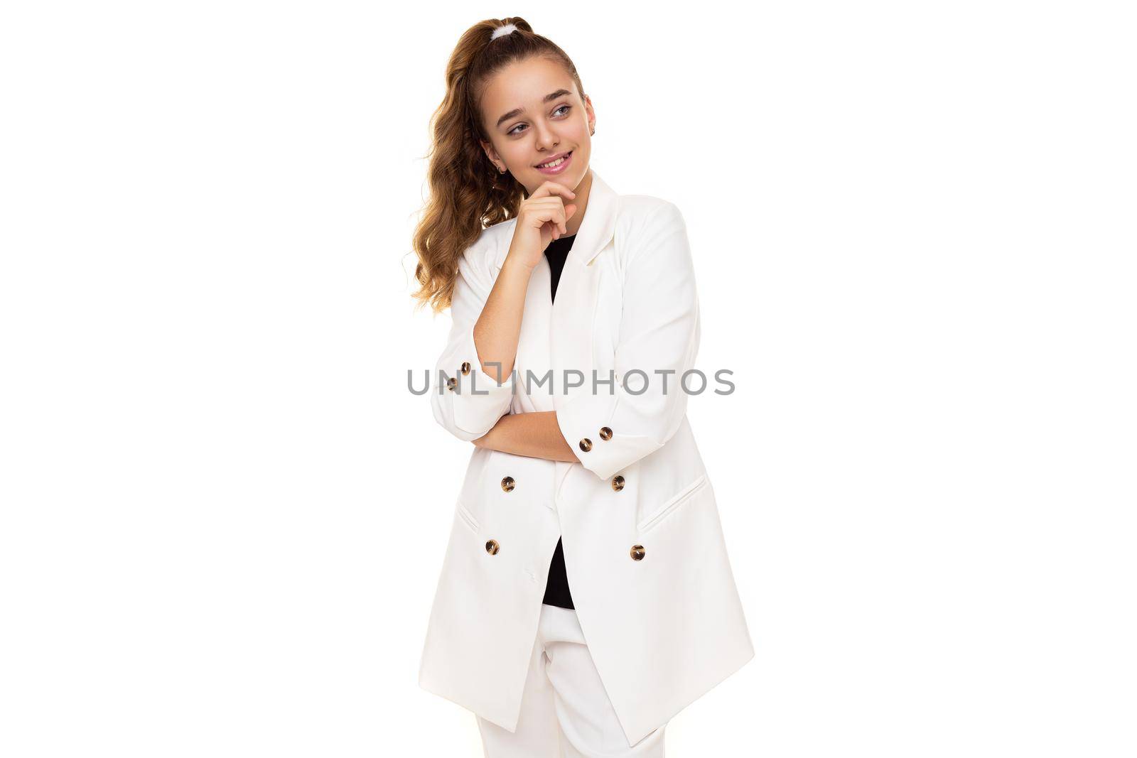 Photo of beautiful cute adorable positive smiling thinking brunette teenage girl with ponytail in stylish white jacket and white pants isolated on white background with copy space for text.