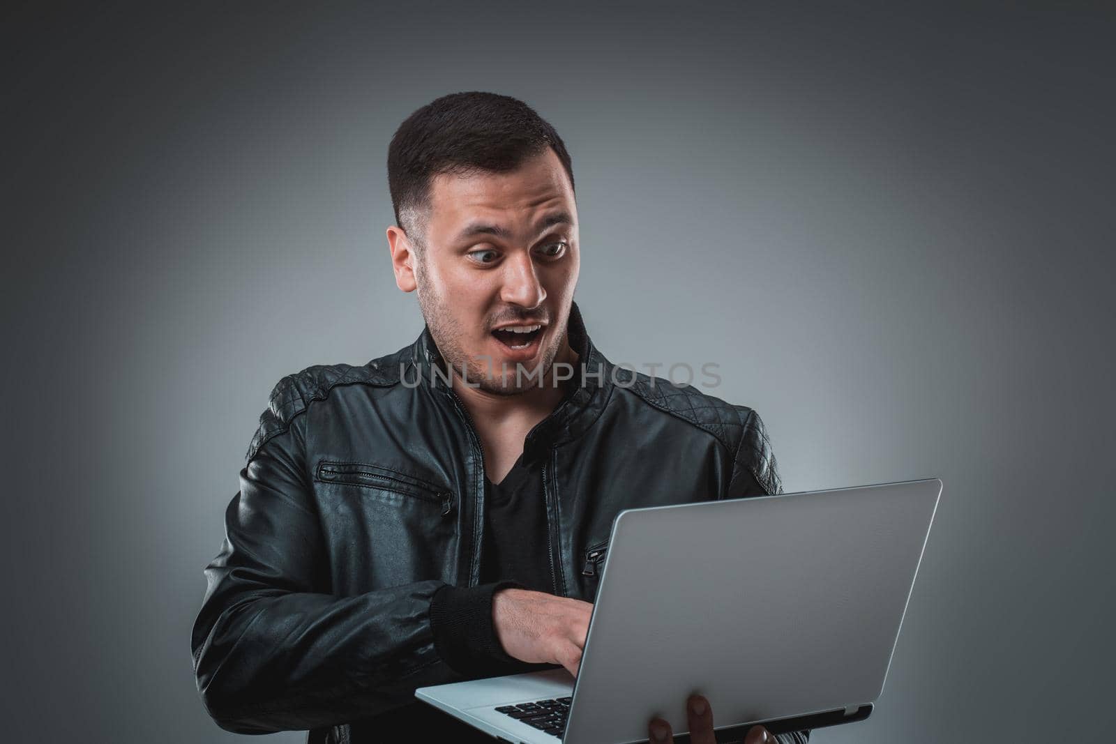 Man in black jacket looking at laptop, half turn. Holding opened laptop and working. Emotion. by nazarovsergey