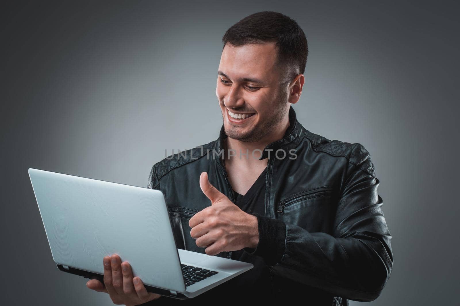 Portrait of young handsome man using laptop, wearing black leather jacket. by nazarovsergey