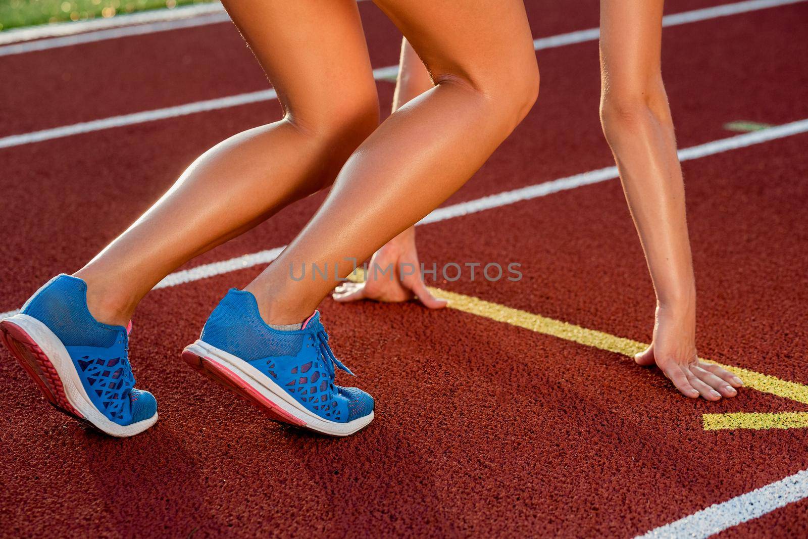 Close-up of woman's legs in blue sneakers on start before jogging. Red treadmill at the stadium