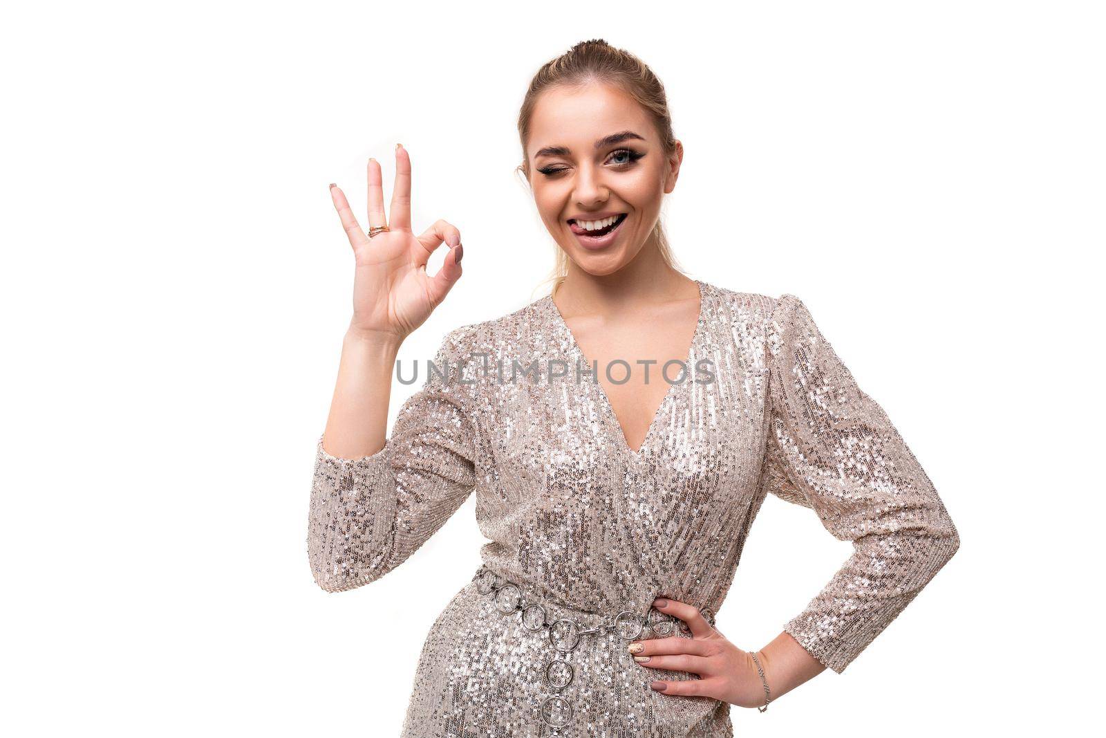 Photo of sexy flirting beautiful attractive charming positive smiling young woman with ponytail and makeup in festive stylish dress with shiny sequins showing ok gesture with hand isolated on white background with free space for text.