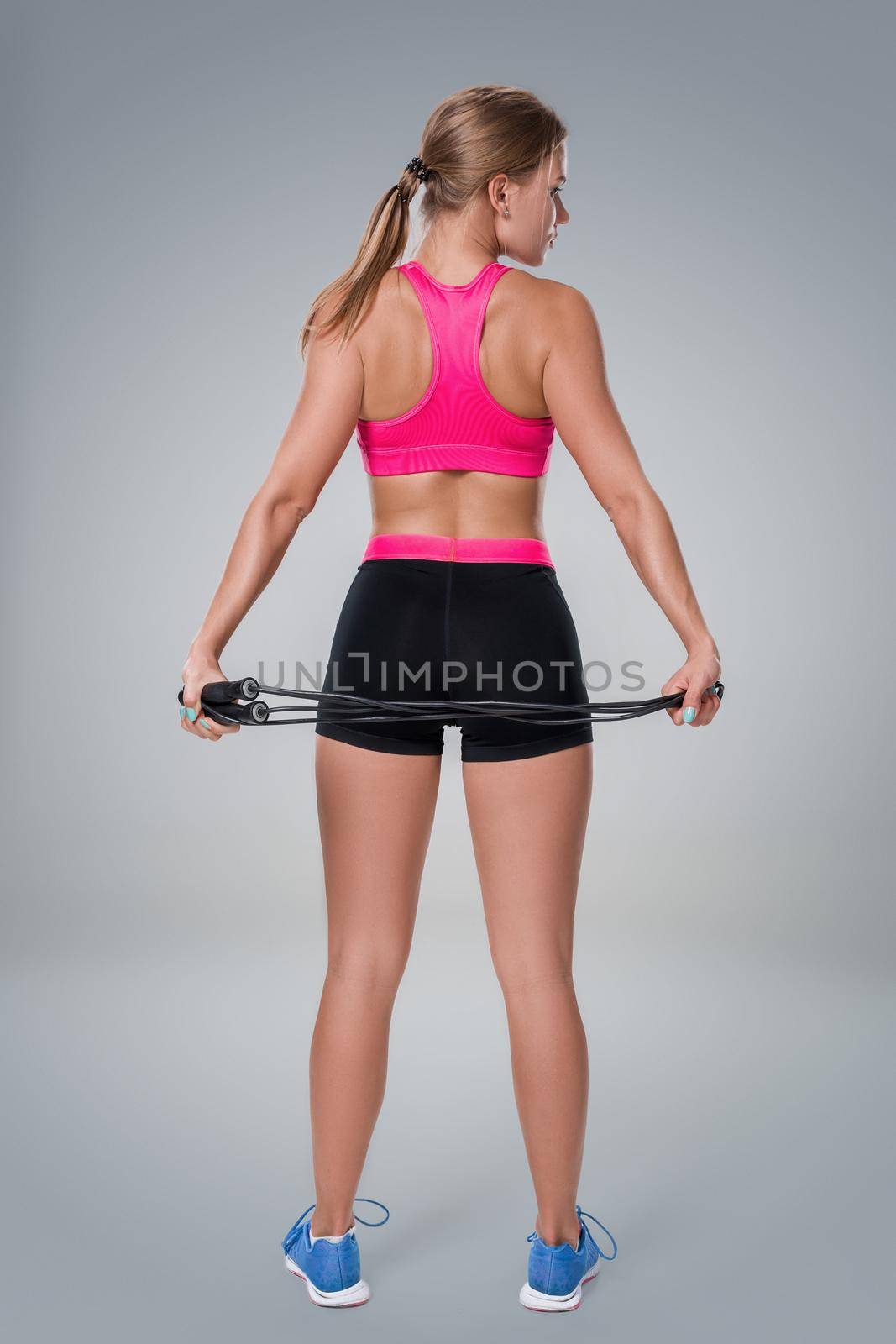 Full length image of a pretty fitness woman doing exercise with skipping rope over gray background by nazarovsergey