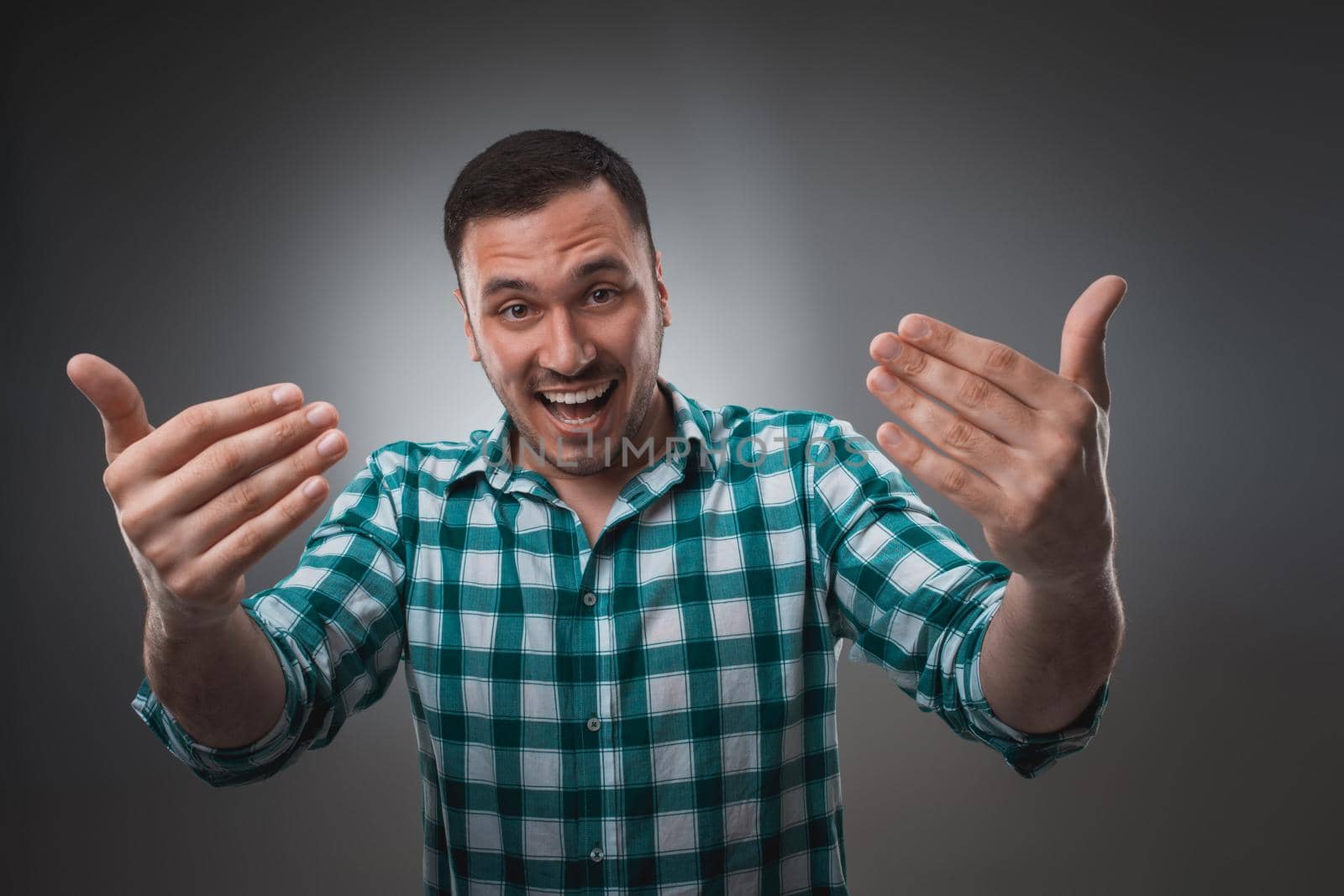 Cheerful man laughing and looking at camera with a big grin. Portrait of a happy young man standing over grey background.