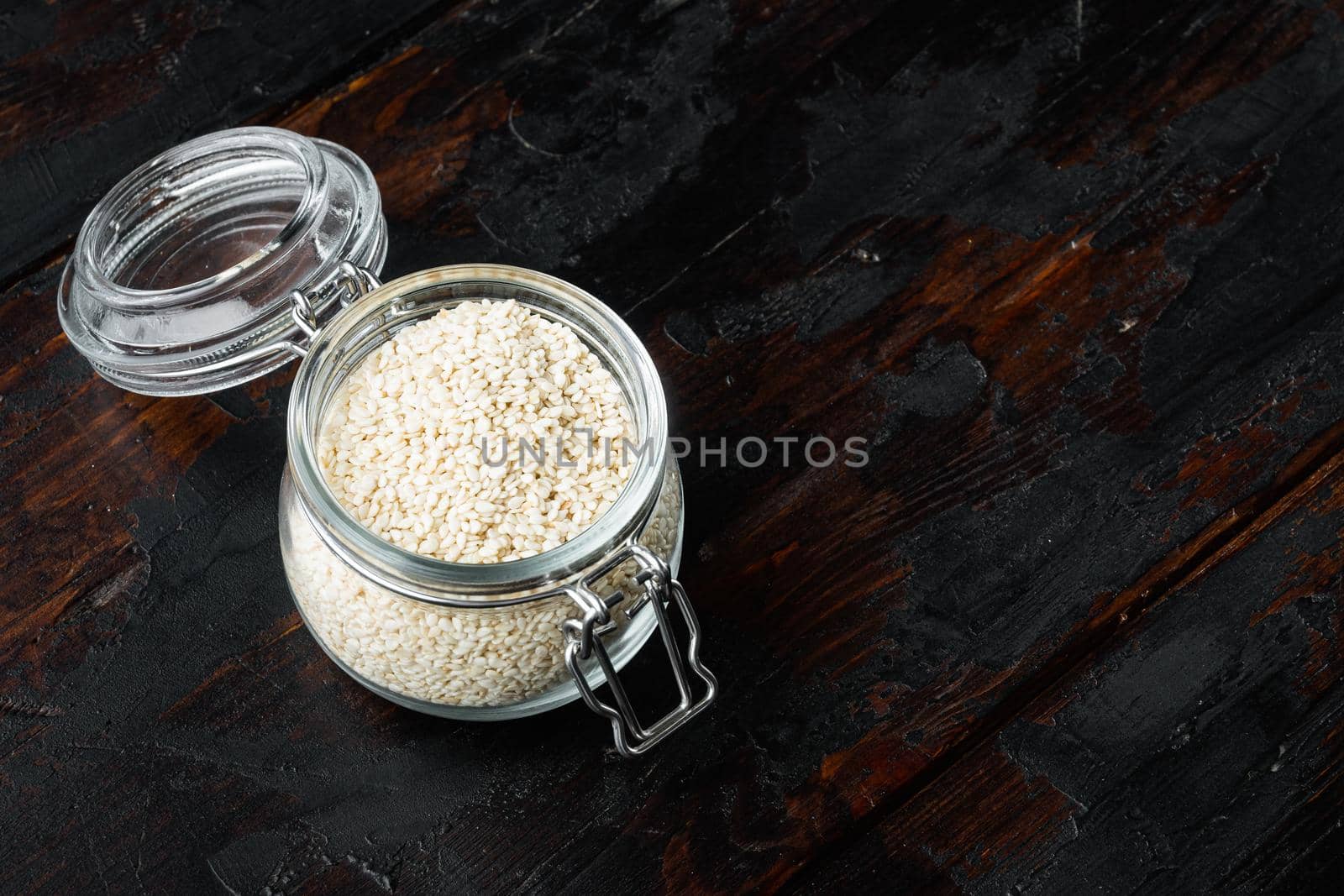 Decorticated sesame seeds set, in glass jar, on old dark wooden table background , with copyspace and space for text